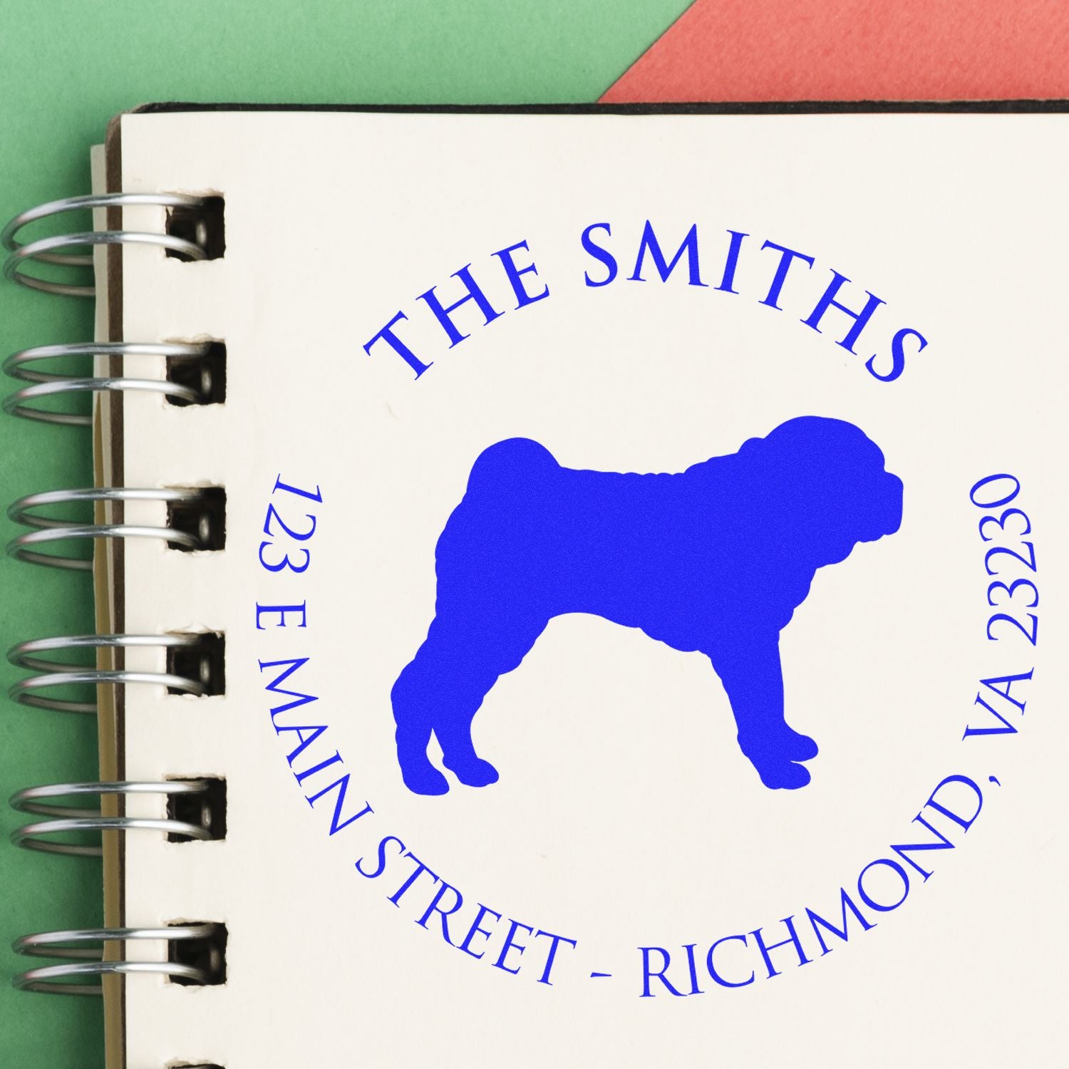 Blue custom stamp seal with dog silhouette and The Smiths address on cream spiral-bound sample page, green and red background.