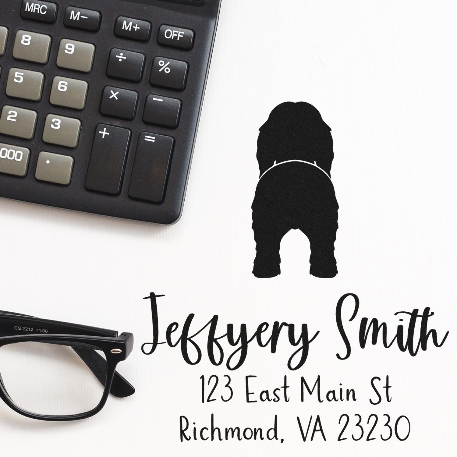 Custom black business stamp and seal with Jeffrey Smith address text on white, beside a black calculator and eyeglasses.
