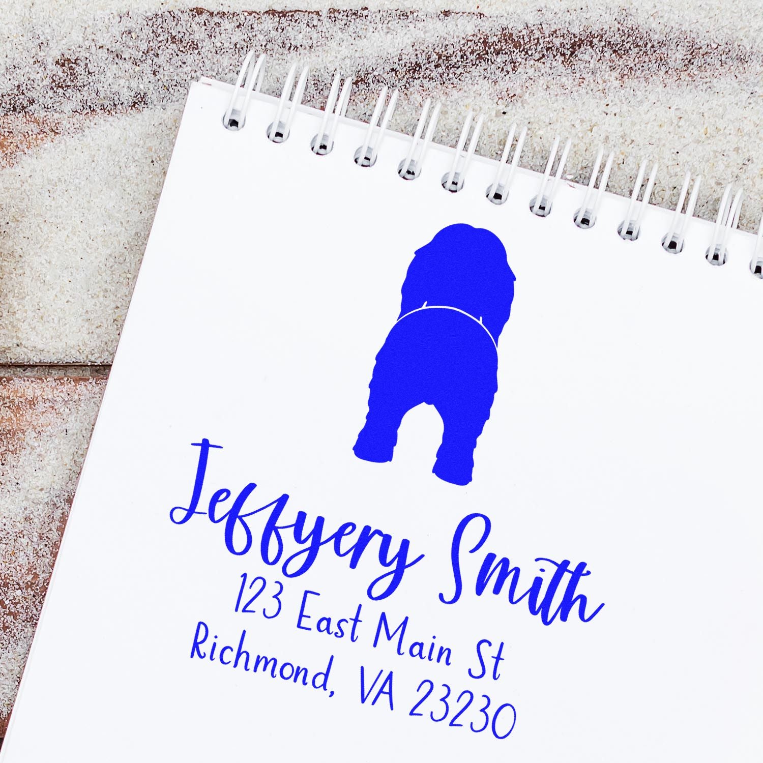 White spiral notepad with blue custom return address stamp and seal, featuring a dog silhouette and name/address.
