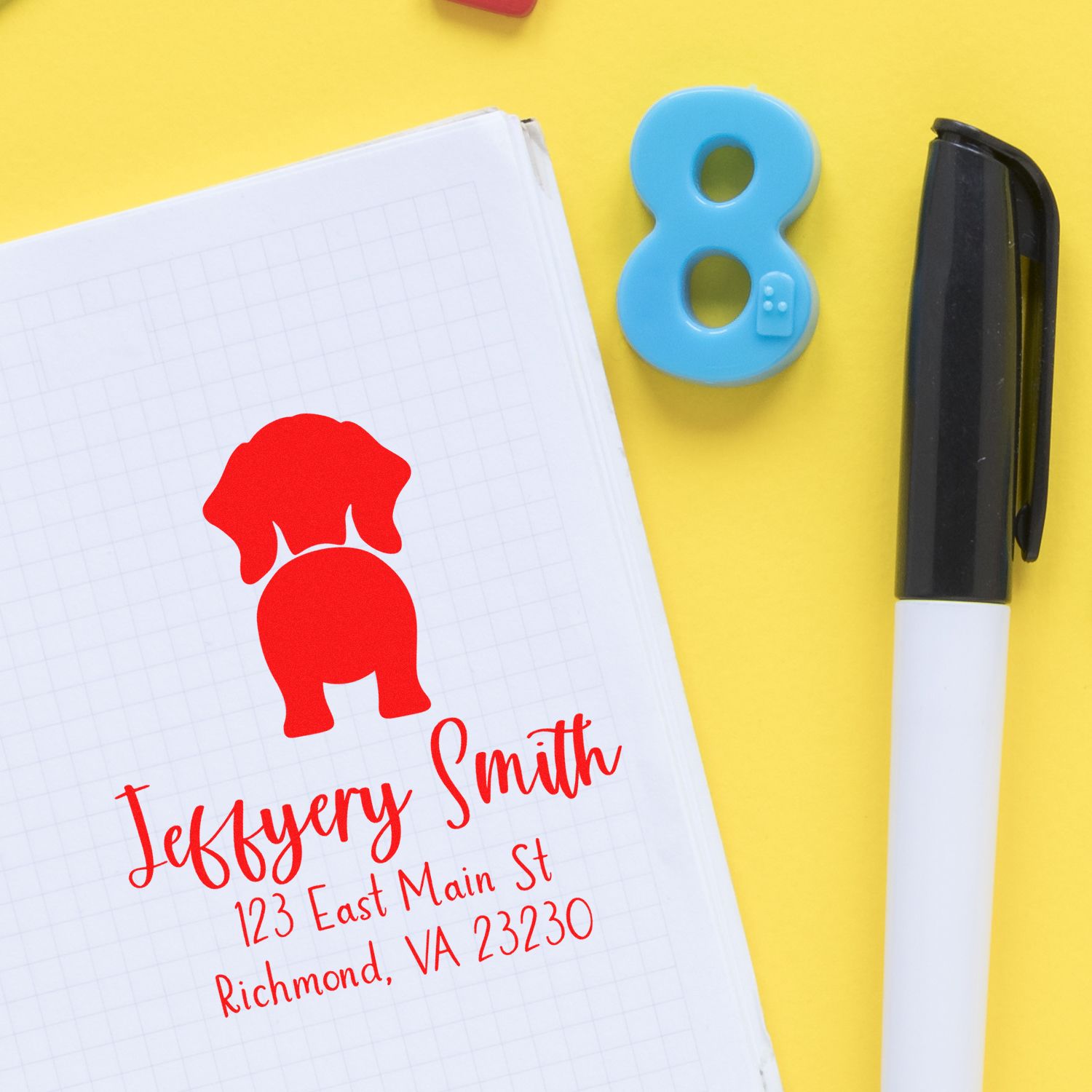 Red custom business seal on a grid notebook, beside a blue number 8 stamp and black marker on a yellow background.