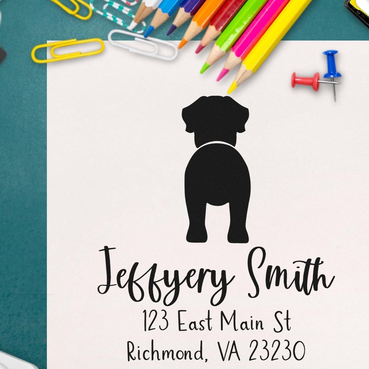 Custom black dog return address stamp and seal design with Jeffery Smith on white paper, surrounded by colorful pencils and paperclips.