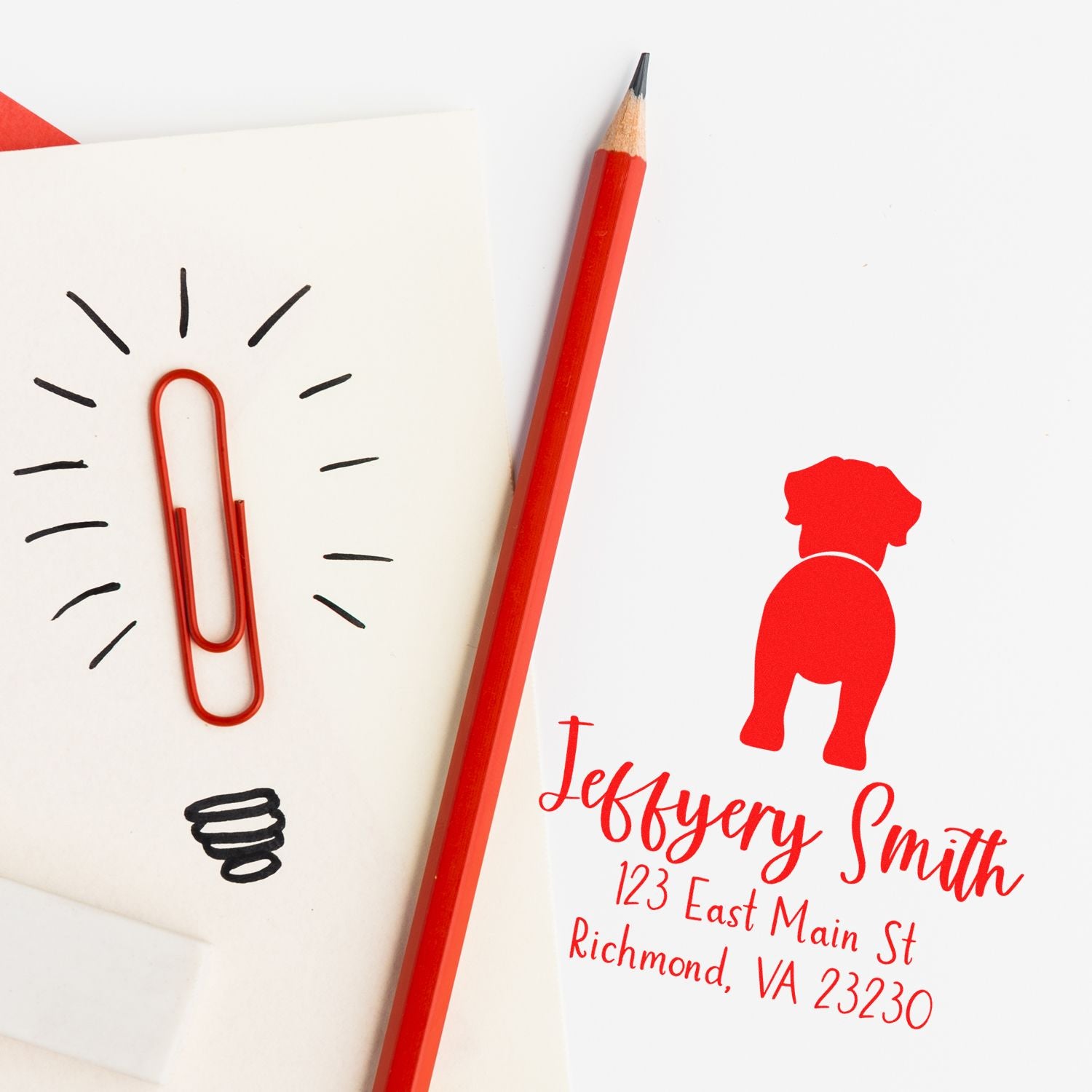 Red custom address stamp and seal with dog silhouette, beside a red pencil and paperclip lightbulb sketch on white cards.