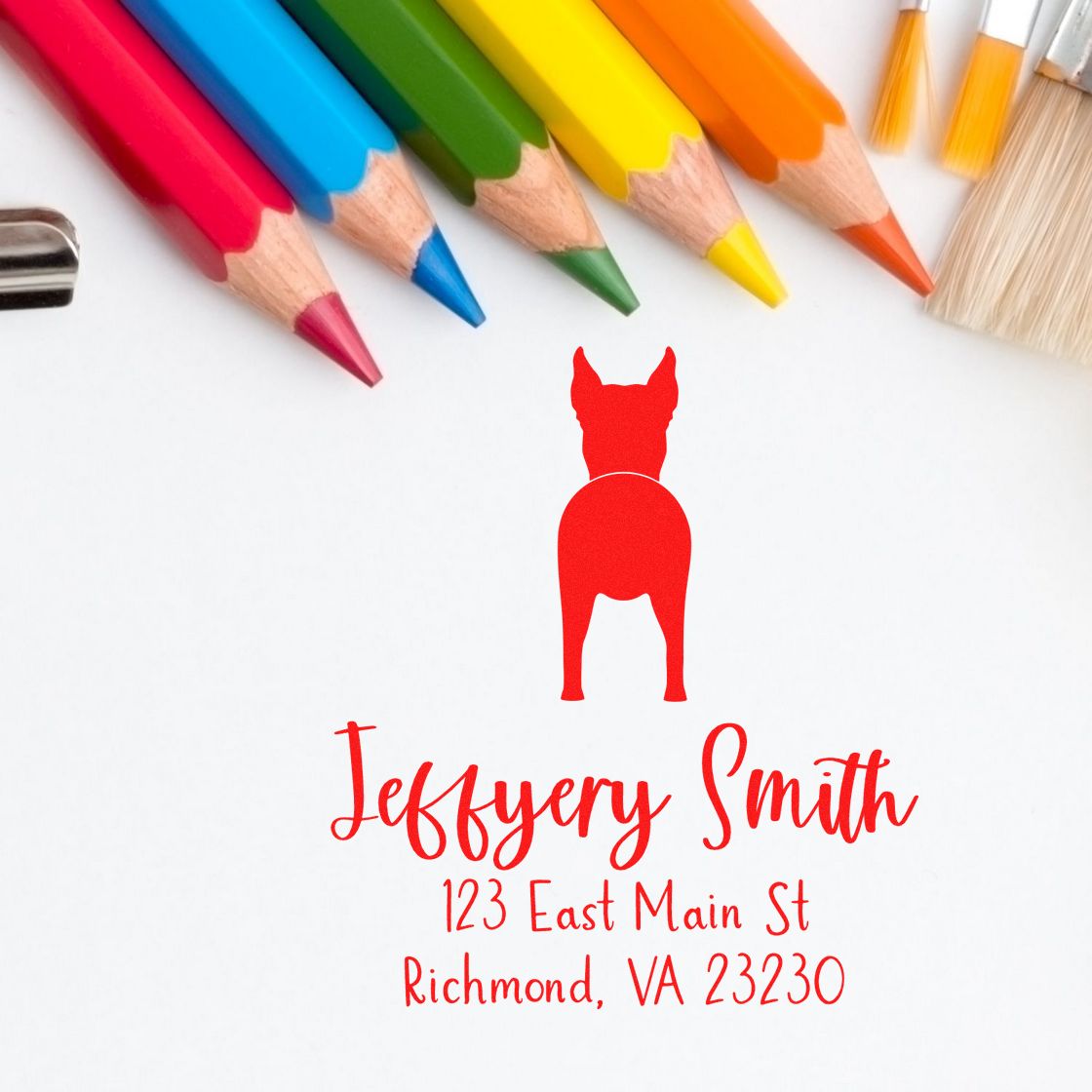 Custom red dog return address stamp and seal with Jeffyery Smith, 123 East Main St, surrounded by colorful pencils and brushes.