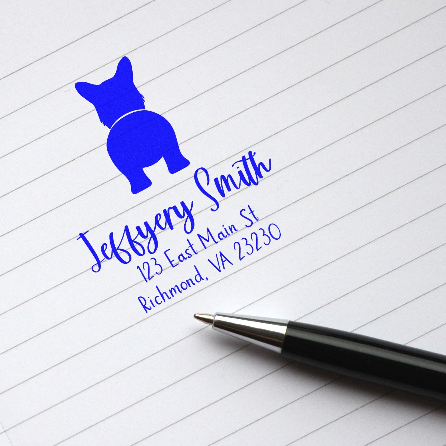 Blue custom address stamp seal with dog logo, Jeffrey Smith name and address on lined paper beside a black pen.