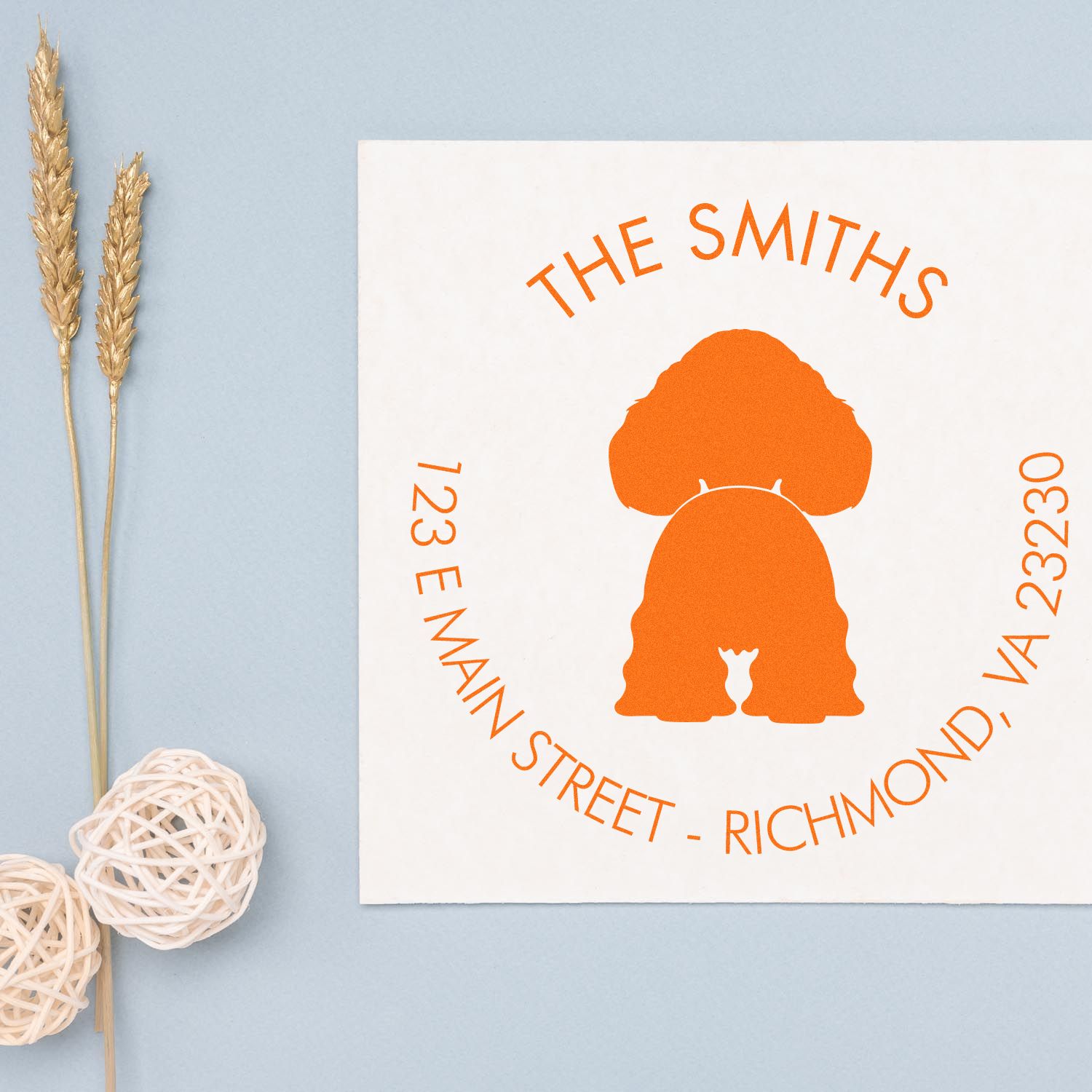 Orange custom stamp seal for The Smiths with address, on white card, styled on pale blue background with gold wheat decor.