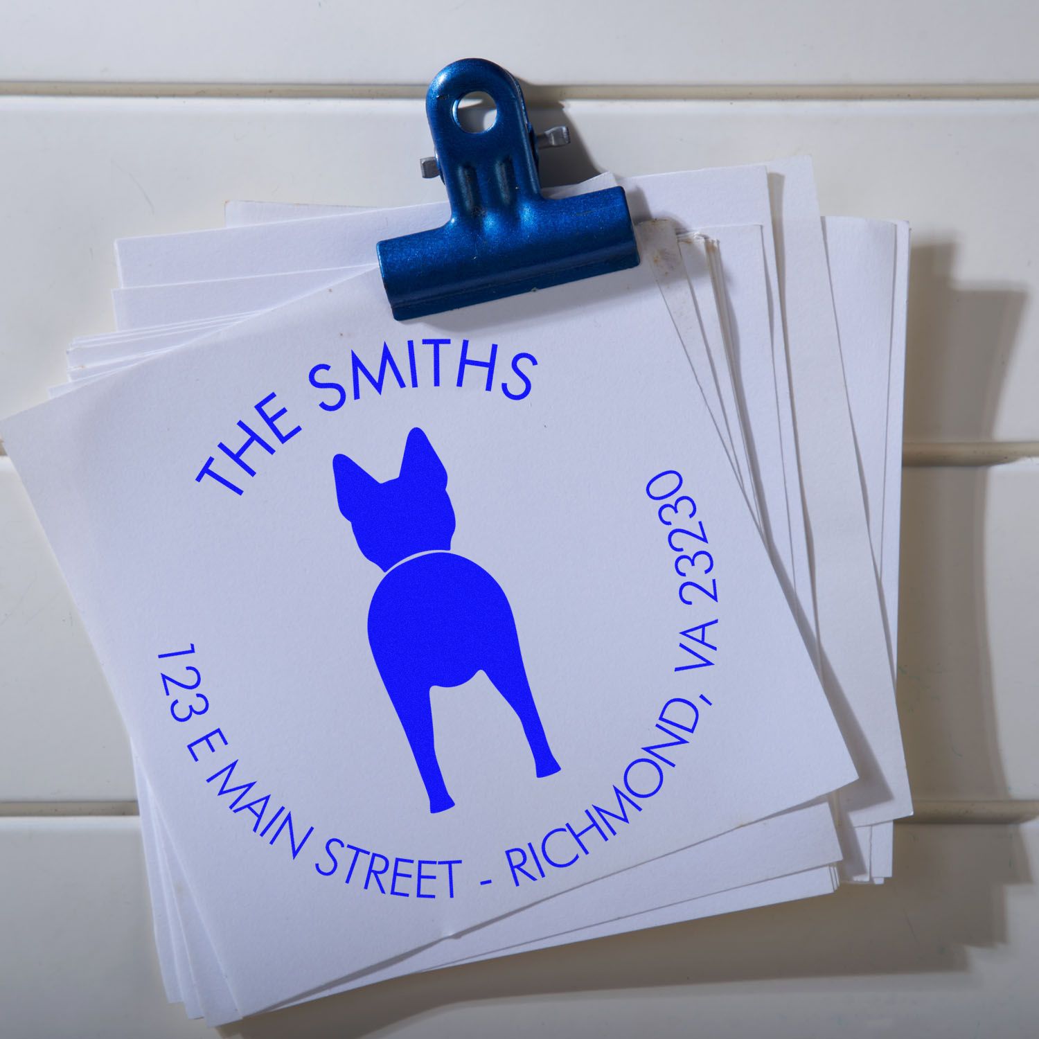 Blue binder clip holding white stamp-and-seal cards with a blue dog logo and The Smiths address
