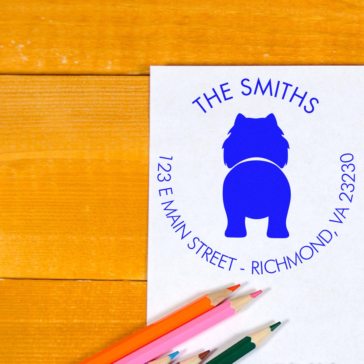 Blue custom stamp seal for The Smiths on white paper, with colorful pencils on a warm wood background.
