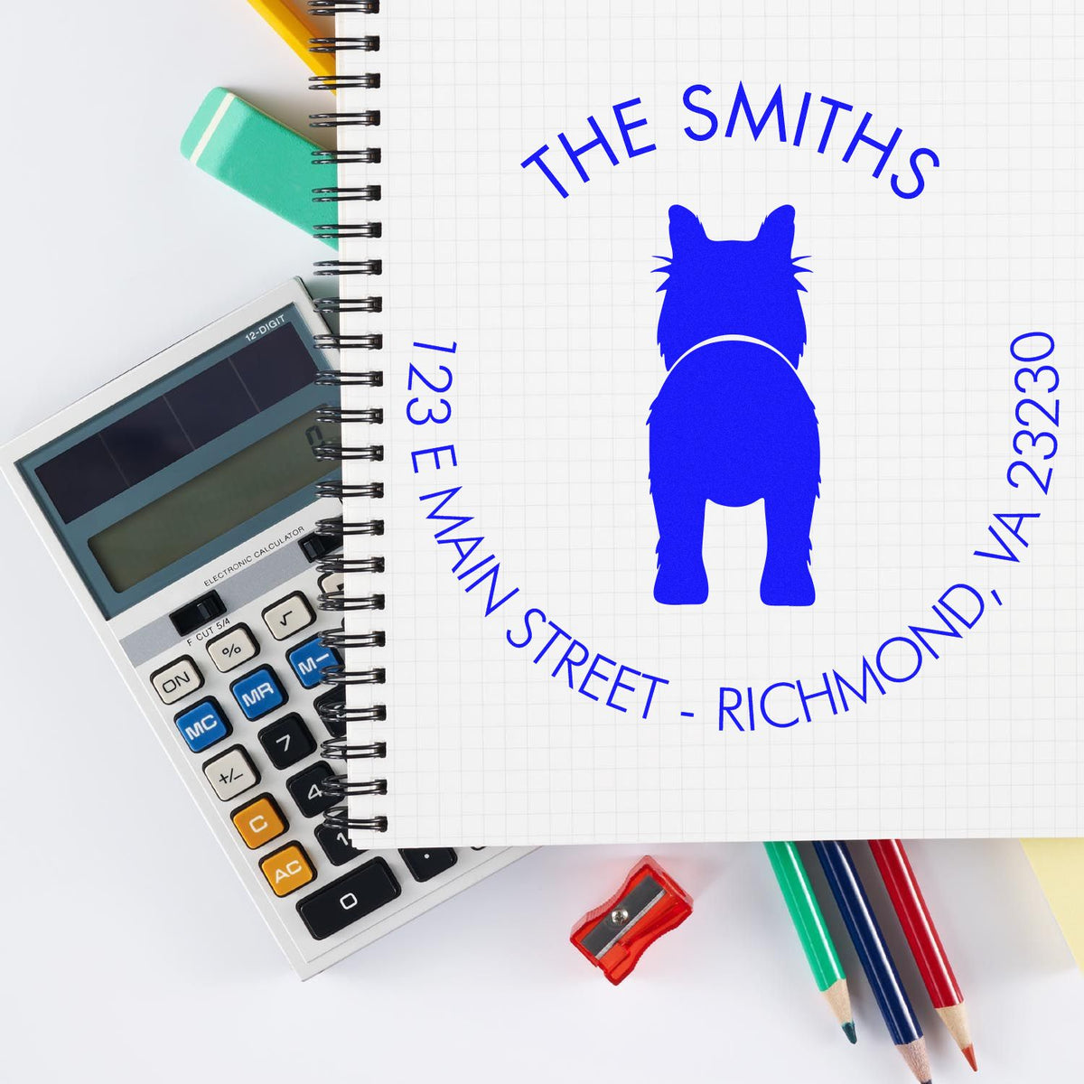Blue custom stamp seal for The Smiths, 123 E Main Street, on notebook beside calculator, sharpener and colored pencils.