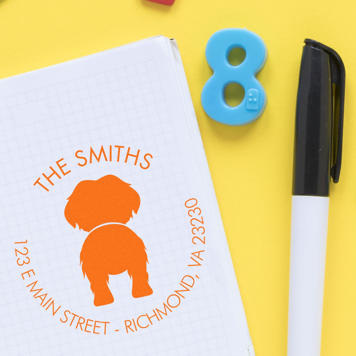 Custom orange address stamp seal on graph paper notebook, with blue number 8 seal and black pen on yellow background.