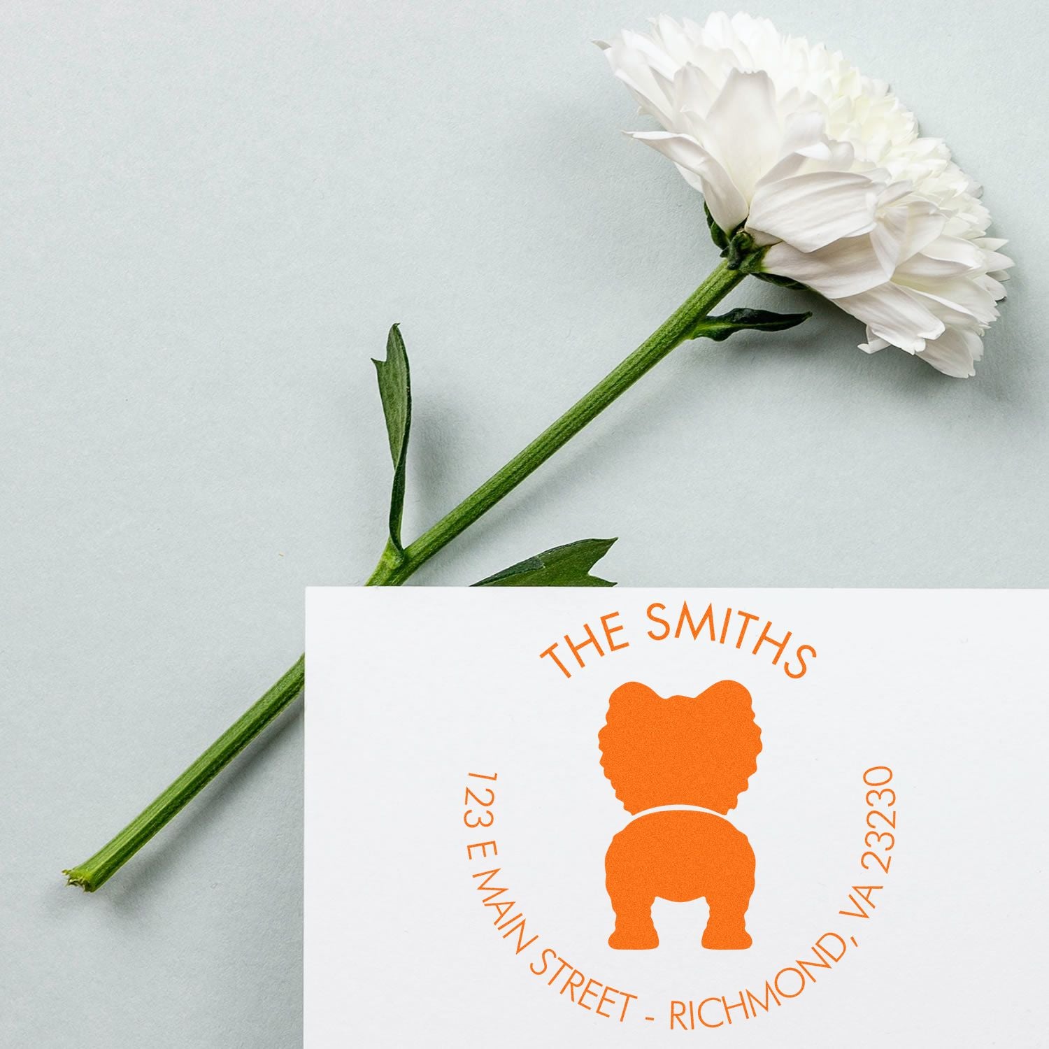 White flower with green stem beside orange custom address stamp seal reading The Smiths.