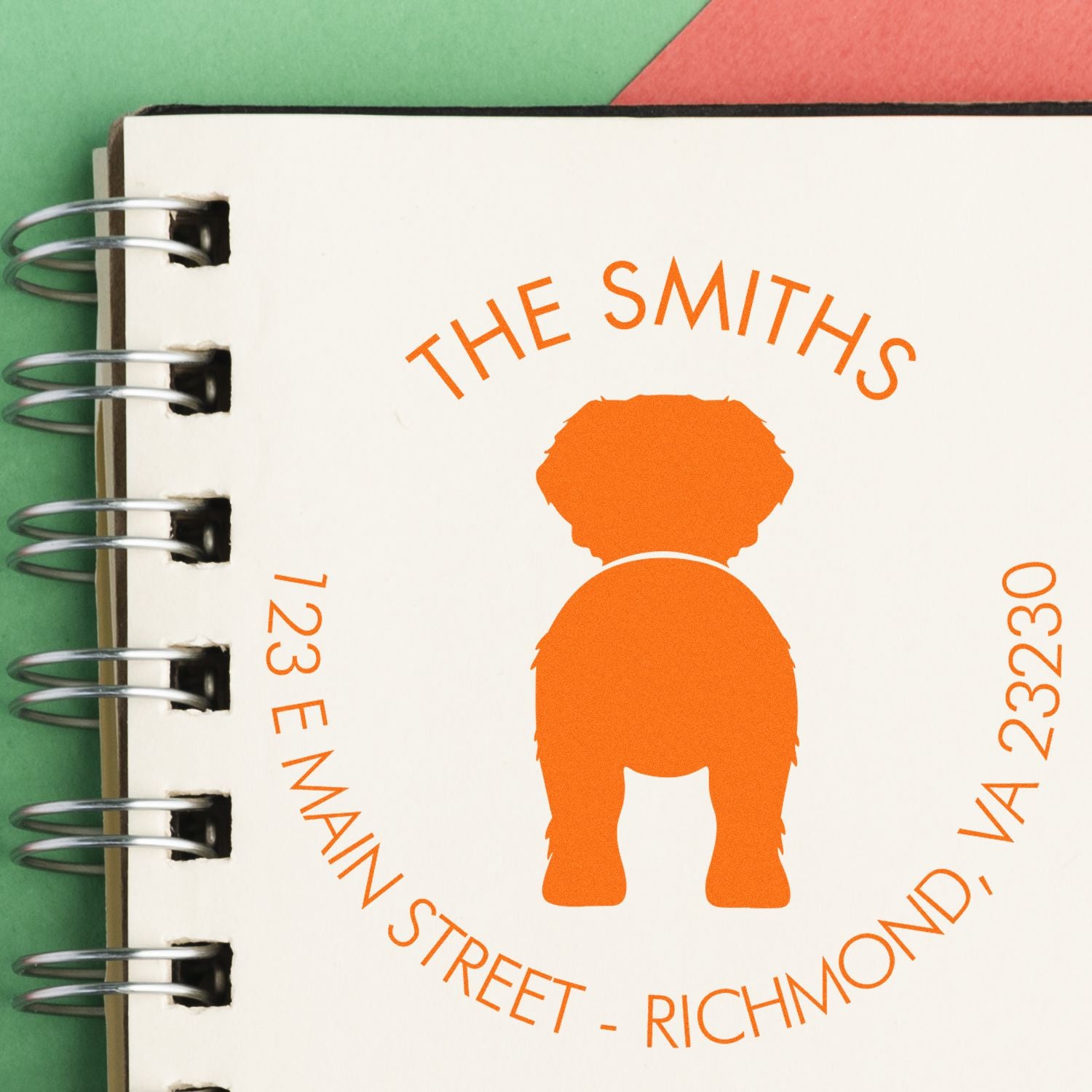 Orange custom stamp and seal for The Smiths, with dog silhouette on a white spiral notebook over green and red background.