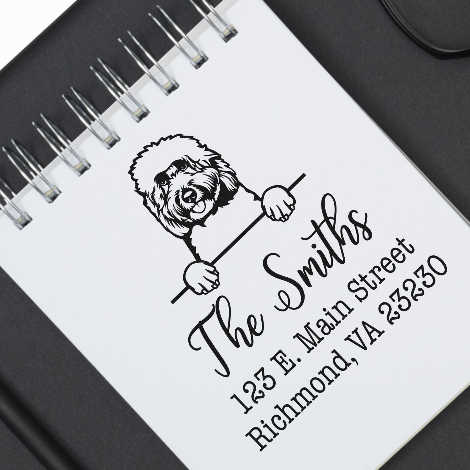 Black custom stamp/seal for The Smiths with dog illustration and address on a white spiral notebook.