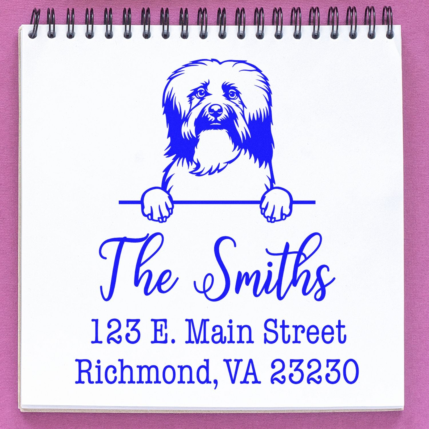 Blue custom address stamp and seal with dog logo, The Smiths, 123 E. Main Street, Richmond, VA 23230 on white notebook.