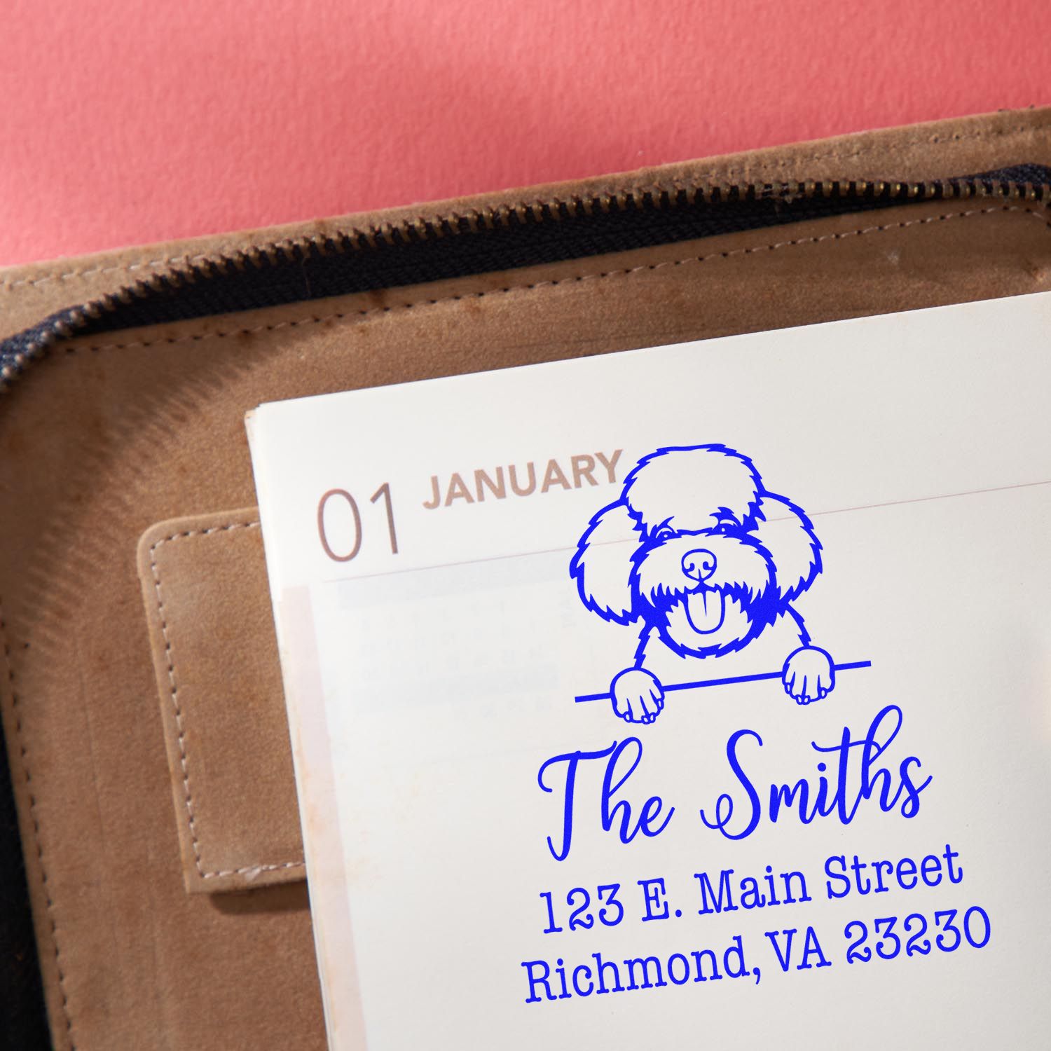 Blue custom dog return address stamp on white planner page, with brown leather zip pouch and pink background.