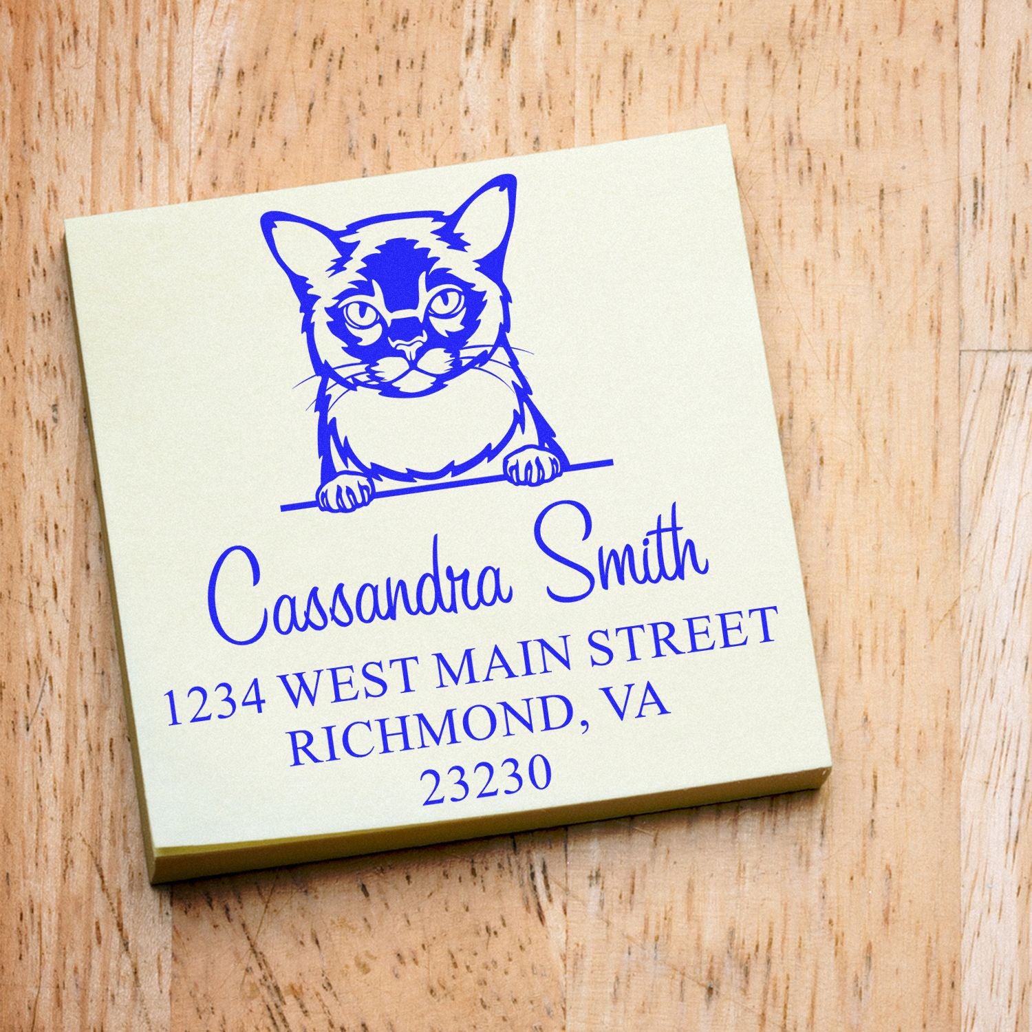 Cream personalized address stamp with blue cat seal, Cassandra Smith, Richmond, VA, on wood background.