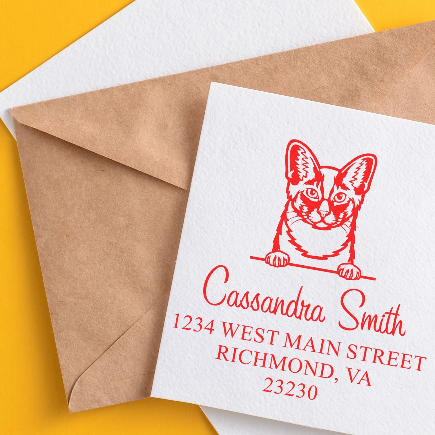 Custom red cat address stamp on white card beside kraft and white envelopes on a yellow background.