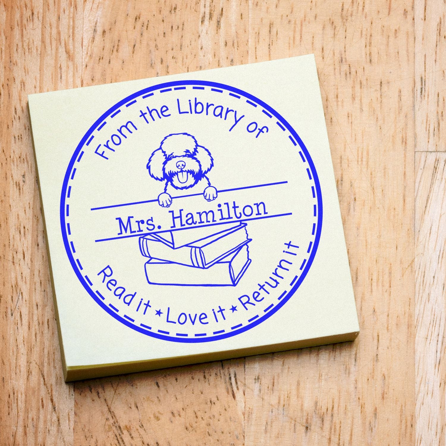 Blue custom library stamp with dog and books, reading From the Library of Mrs. Hamilton, on a cream pad.