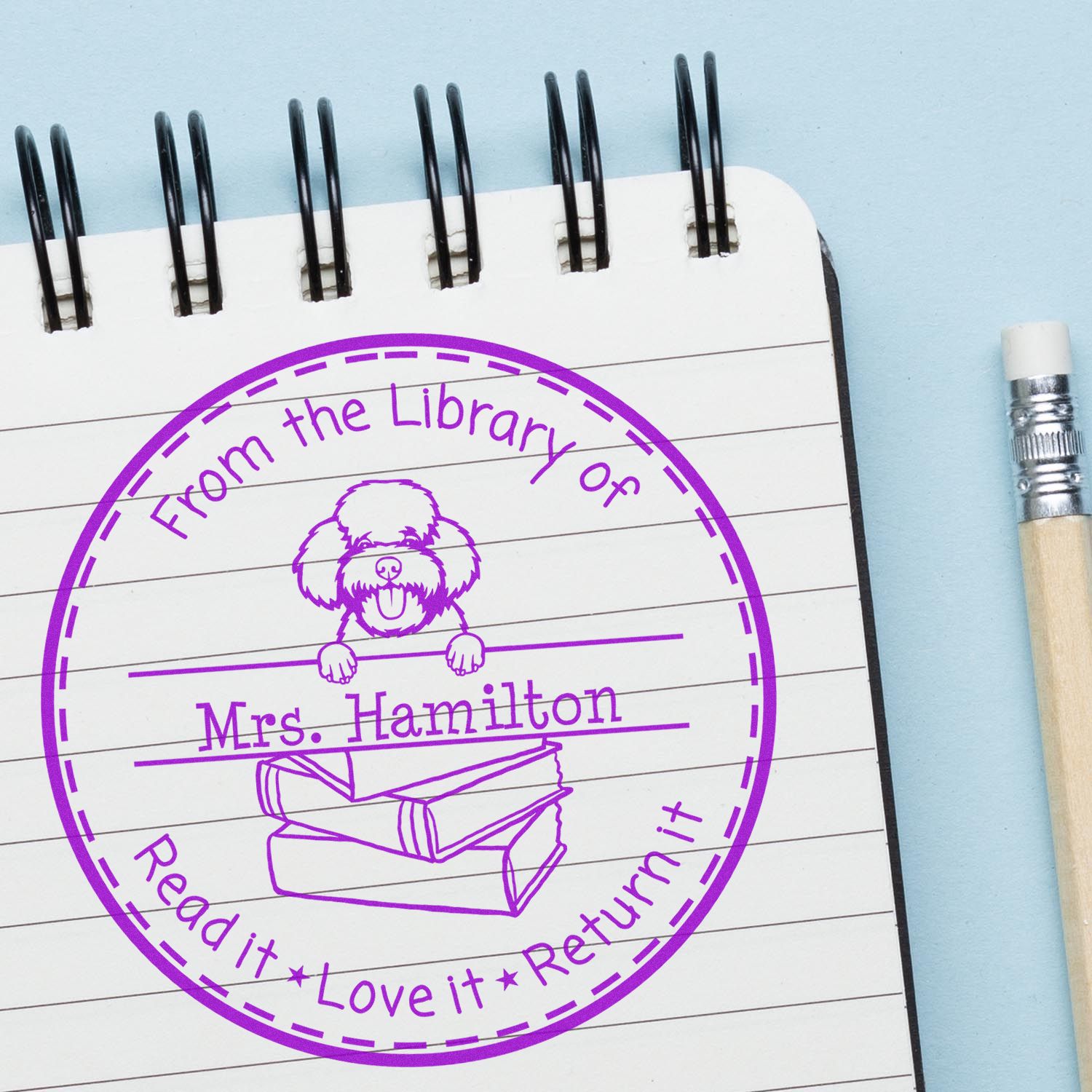 Purple circular library return stamp seal on notepad, with dog and books, labeled Mrs. Hamilton, beside a pencil.