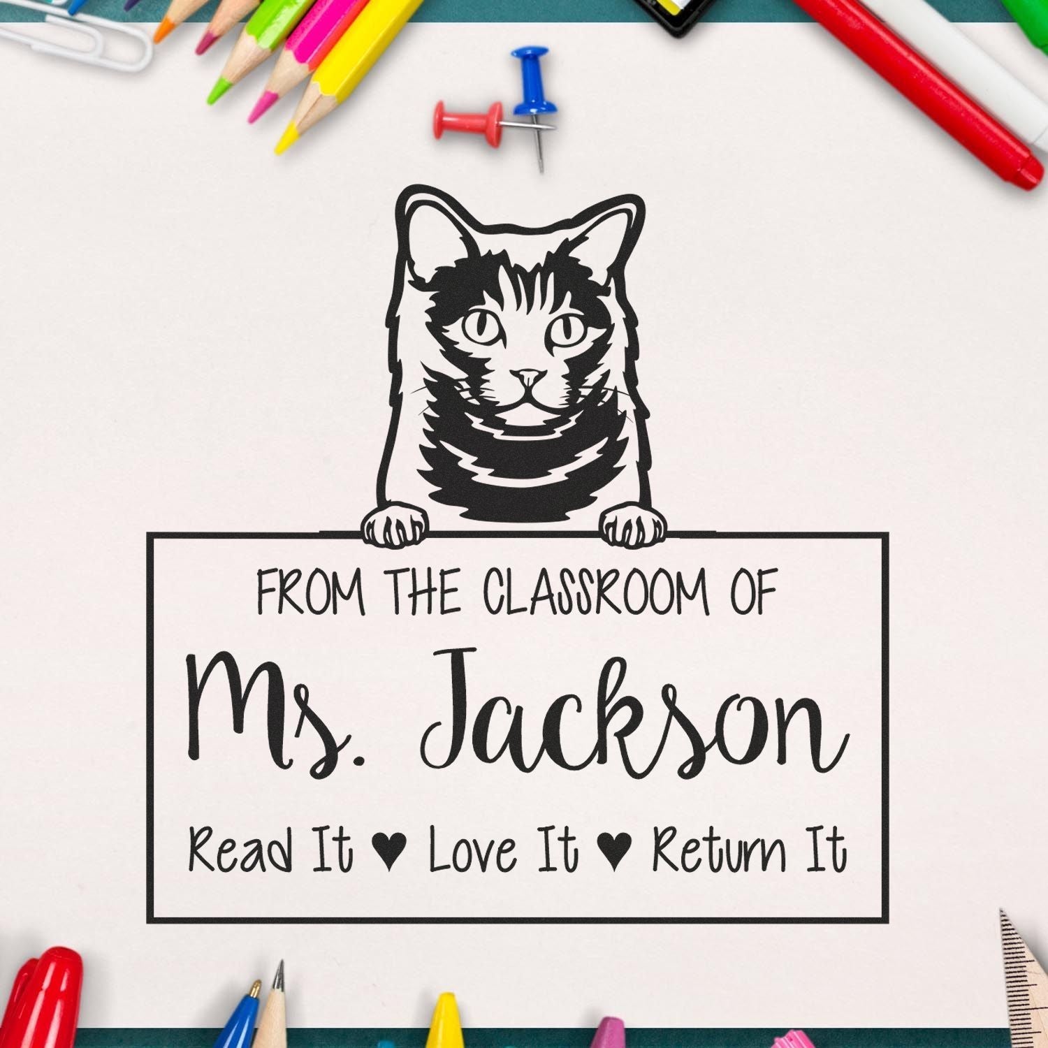Black cat classroom stamp seal with From the Classroom of Ms. Jackson, surrounded by colorful pencils and pins on white paper.