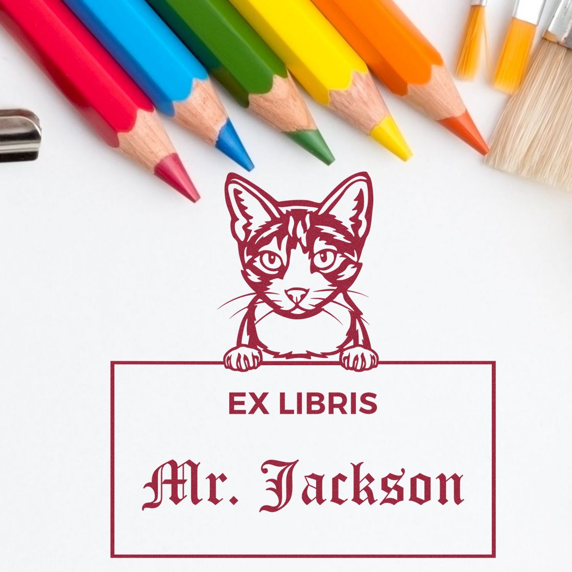Red ex libris stamp and book seal with cat illustration and Mr. Jackson, framed by colorful pencils on white.