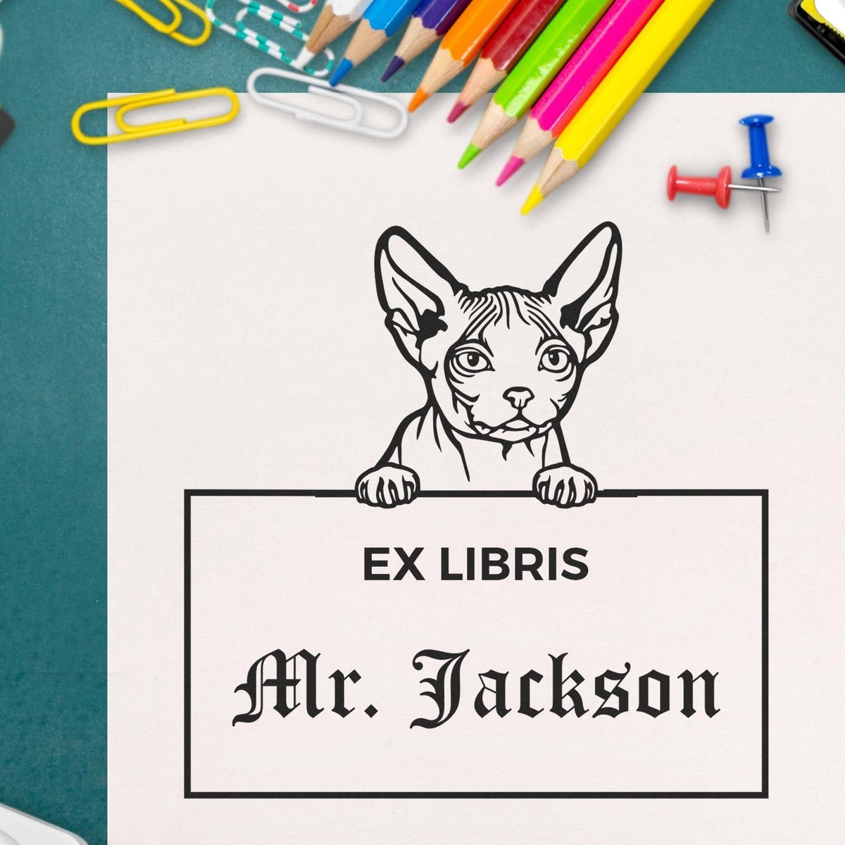 Custom ex libris stamp and seal with black dog illustration and Mr. Jackson text on white paper, with colorful pencils and clips.