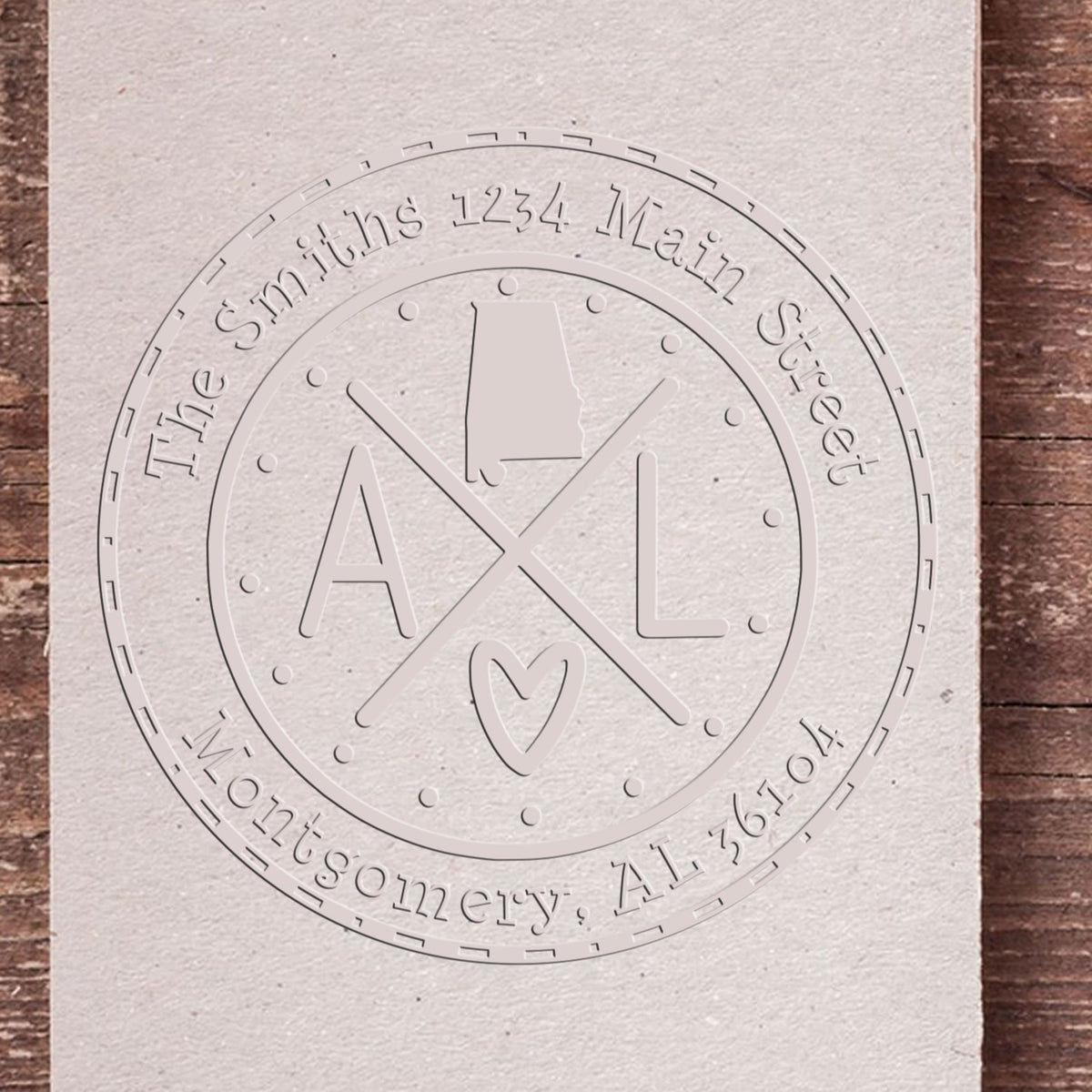 Embossed silver-gray custom stamp seal with AL monogram, Montgomery, AL 36104, on textured paper.
