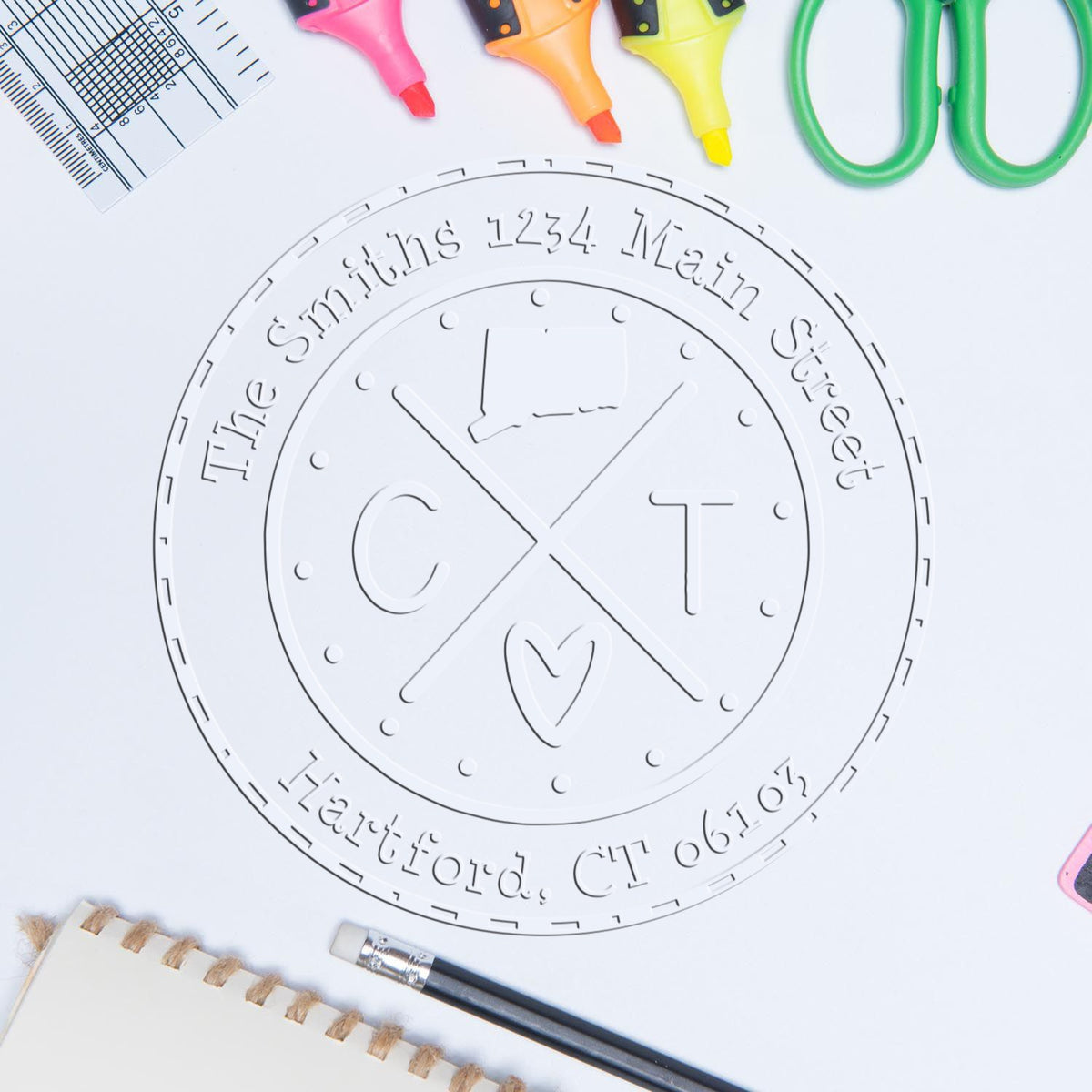 White custom embossing seal stamp for CT address, surrounded by colorful highlighters, ruler, scissors, and pencil.