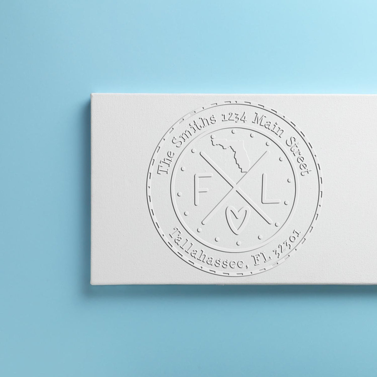 White embossed custom stamp seal with circular monogram and address text on a light blue background.