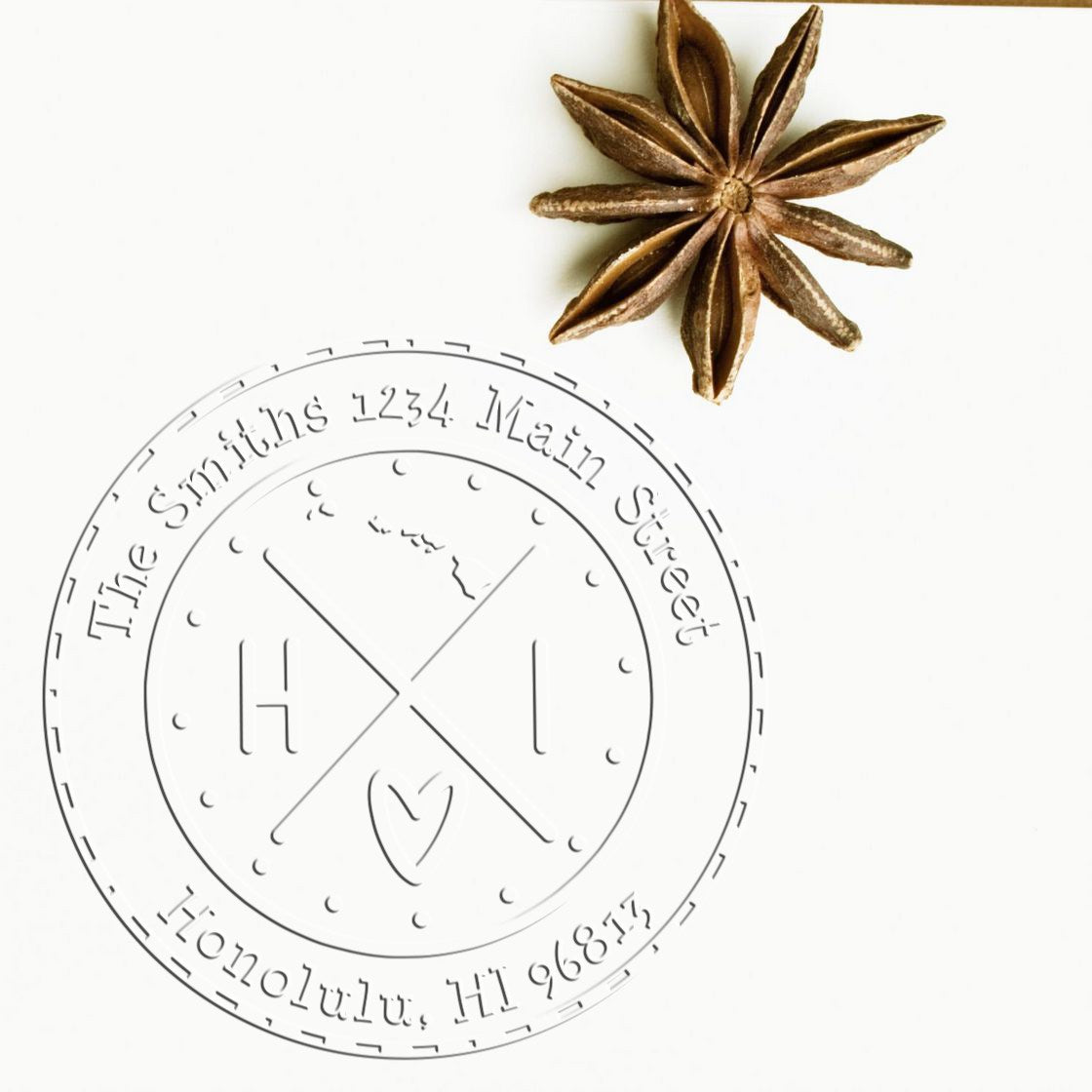 Light gray circular embossing seal stamp on white, with brown star anise accent and custom text around the edge.