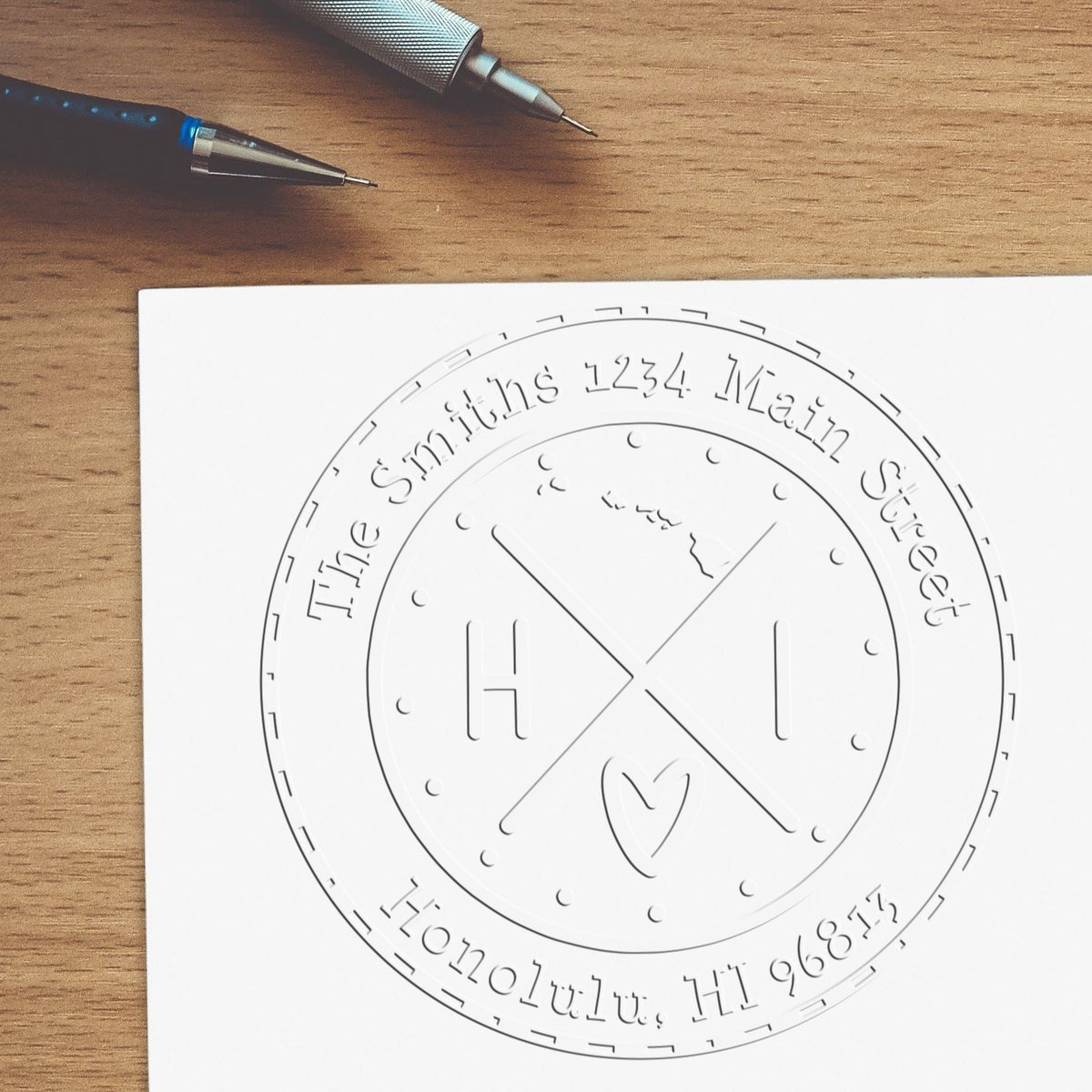 Custom round white stamp and seal design with embossed HI initials, heart, and address on a wood desk with pens.