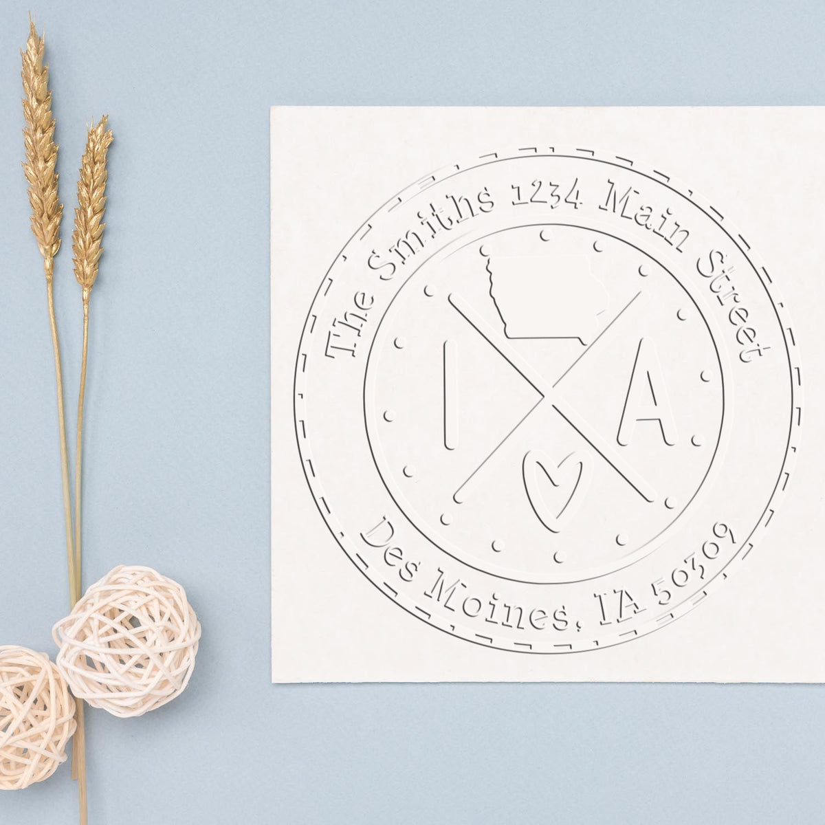 Custom round white embossing seal stamp on pale blue background, accented with gold wheat stems and woven white decor balls.