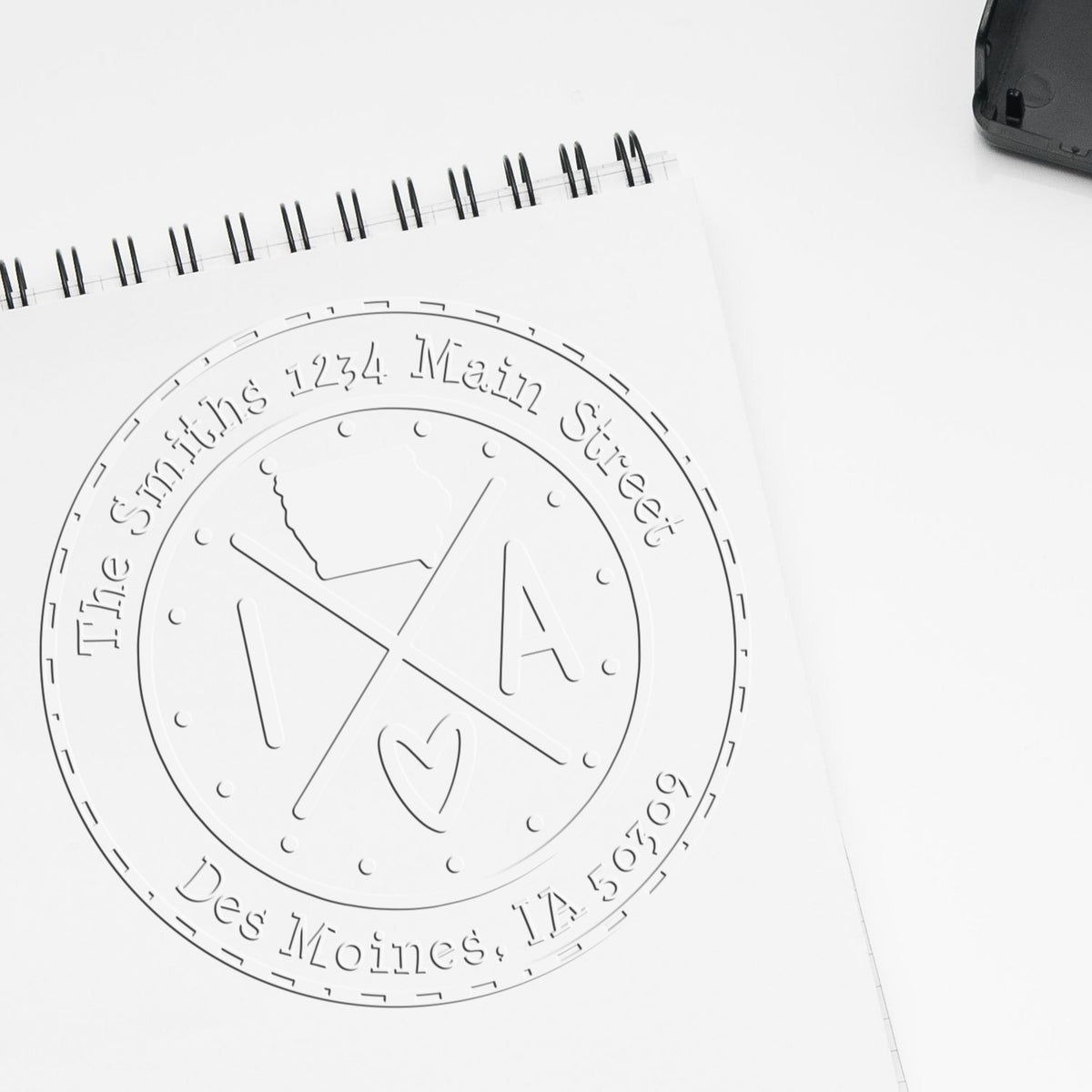 White embossed custom stamp seal on a spiral notebook, featuring The Smiths, 1234 Main Street, Des Moines, IA 50309.