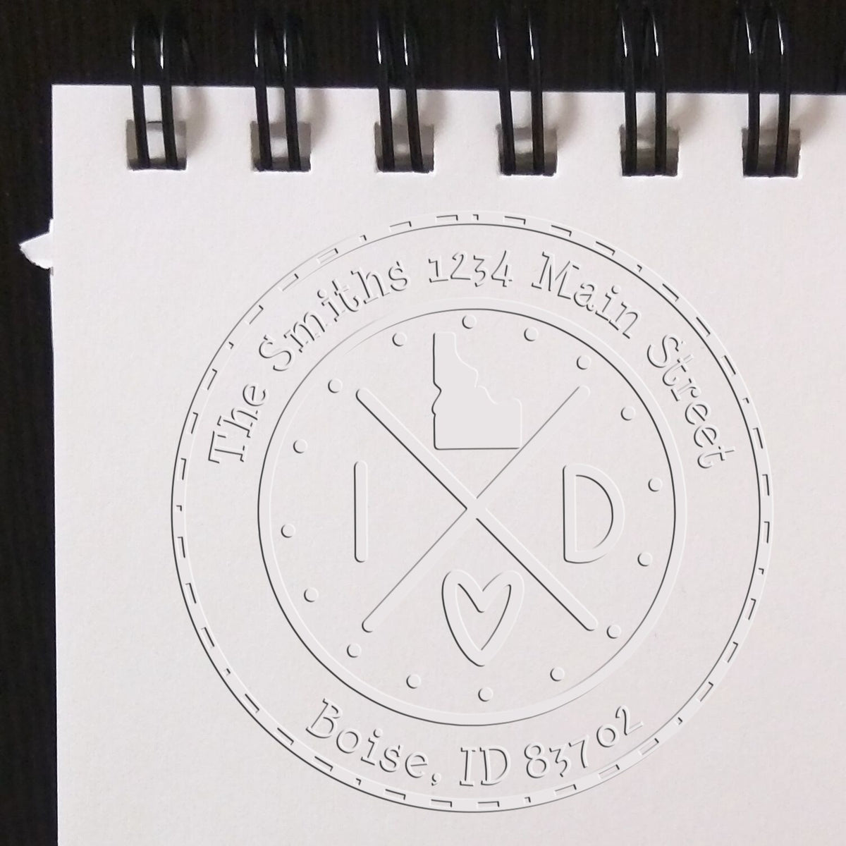 Embossed round address seal stamp in white, with black notebook rings, reading The Smiths, 1234 Main Street, Boise, ID 83702.