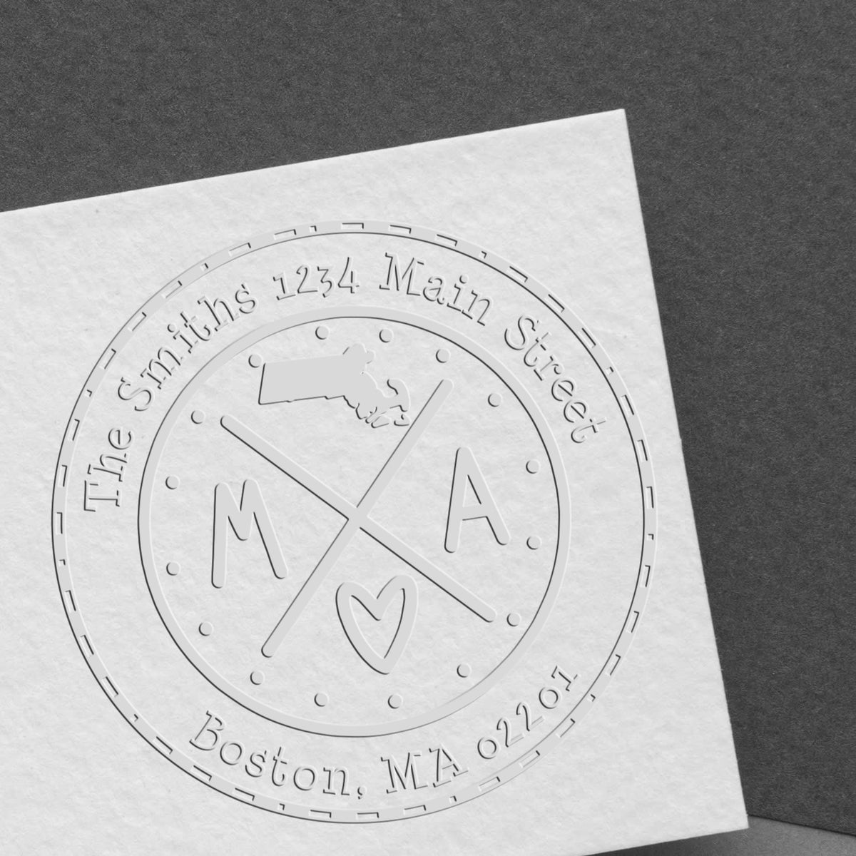 Embossed white custom stamp seal with M A monogram, heart, and Boston address on textured paper.