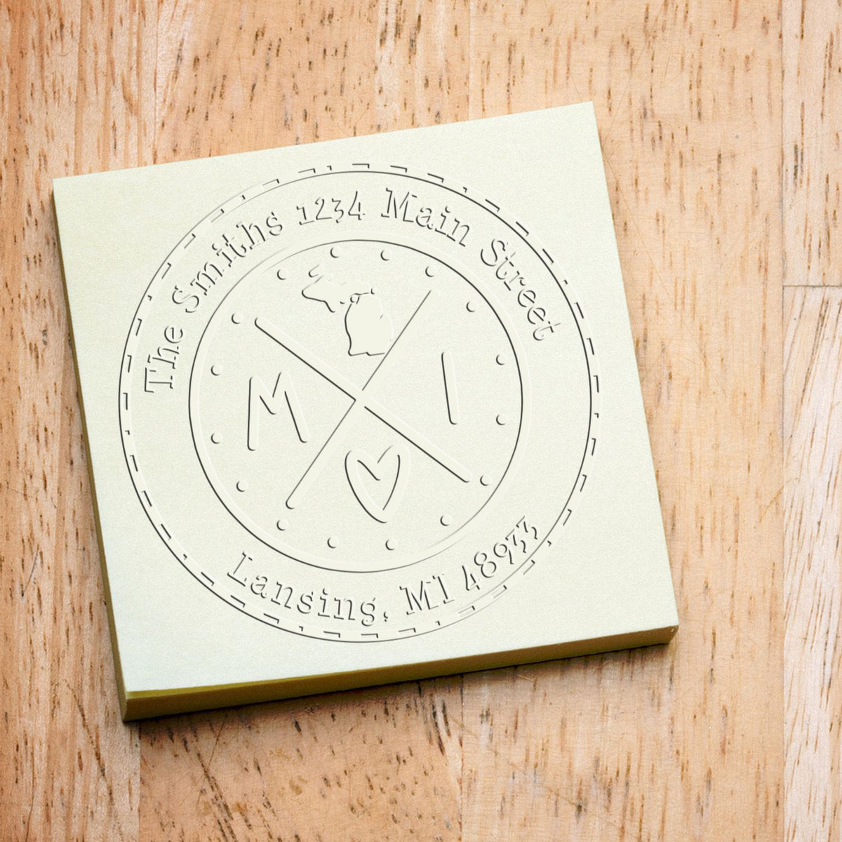 Cream custom embossing stamp seal with circular monogram and address, on a wood-grain background.