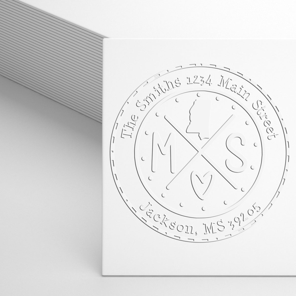 White embossed custom stamp seal with initials M S and address text on a white card.