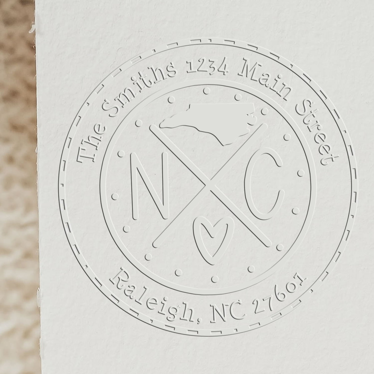 Embossed white circular stamp seal for The Smiths, 1234 Main Street, Raleigh, NC 27601, with NXC and heart.