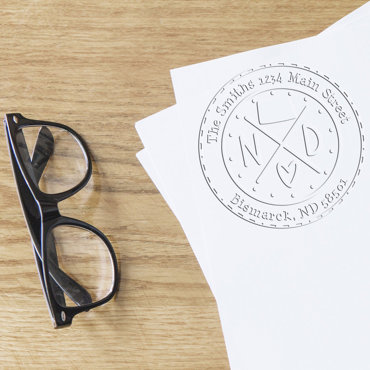 Black eyeglasses beside white sheets with a circular custom stamp and seal design on a light wood tabletop.
