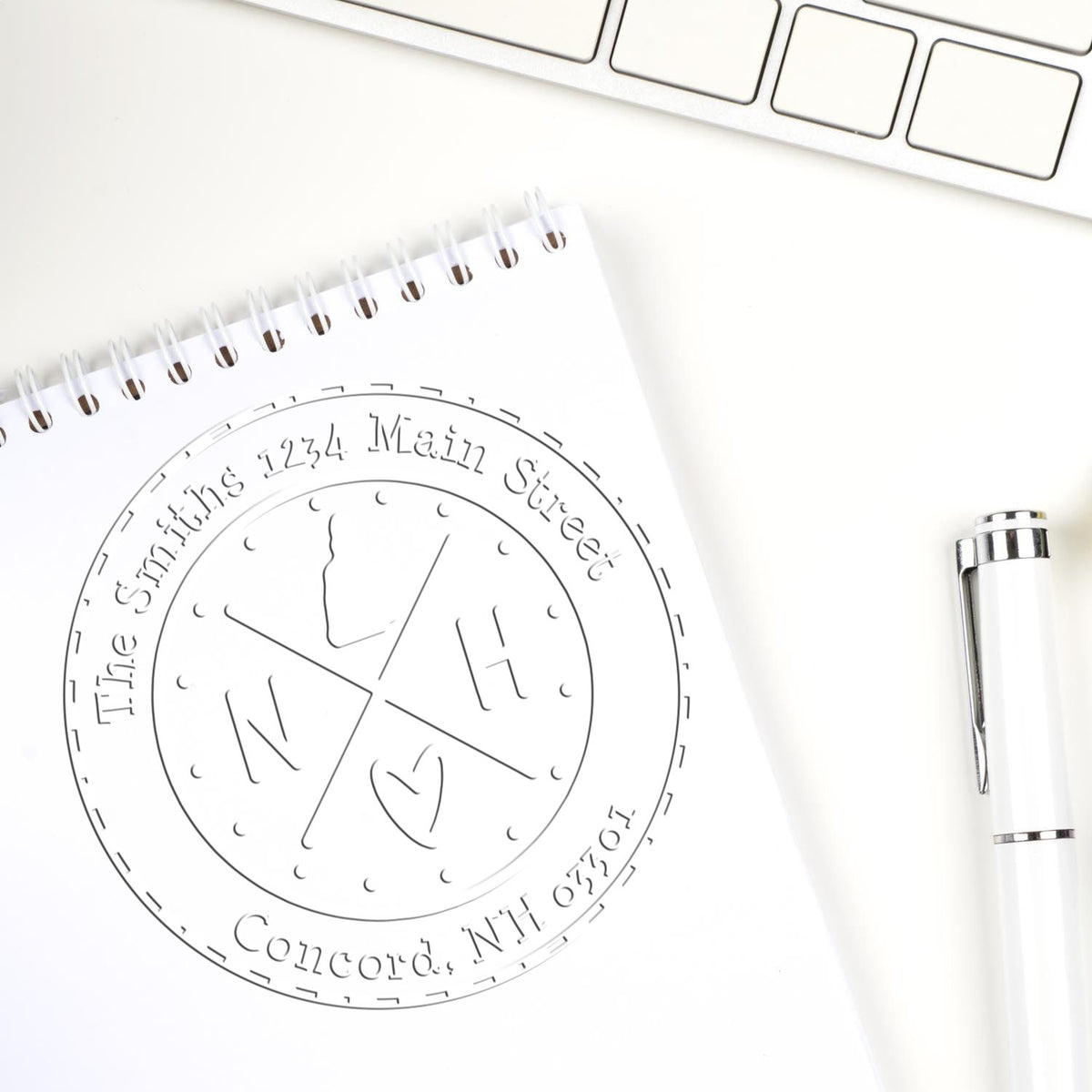 Custom round stamp seal design on a white spiral notepad, with silver pen and keyboard edge on a clean white desk