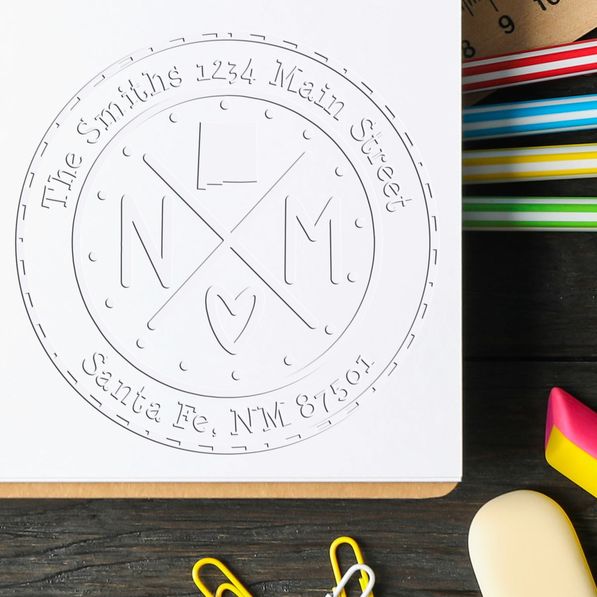 White circular custom stamp seal with embossed Smiths address text and NM monogram, beside colorful ink pads on a dark desk.