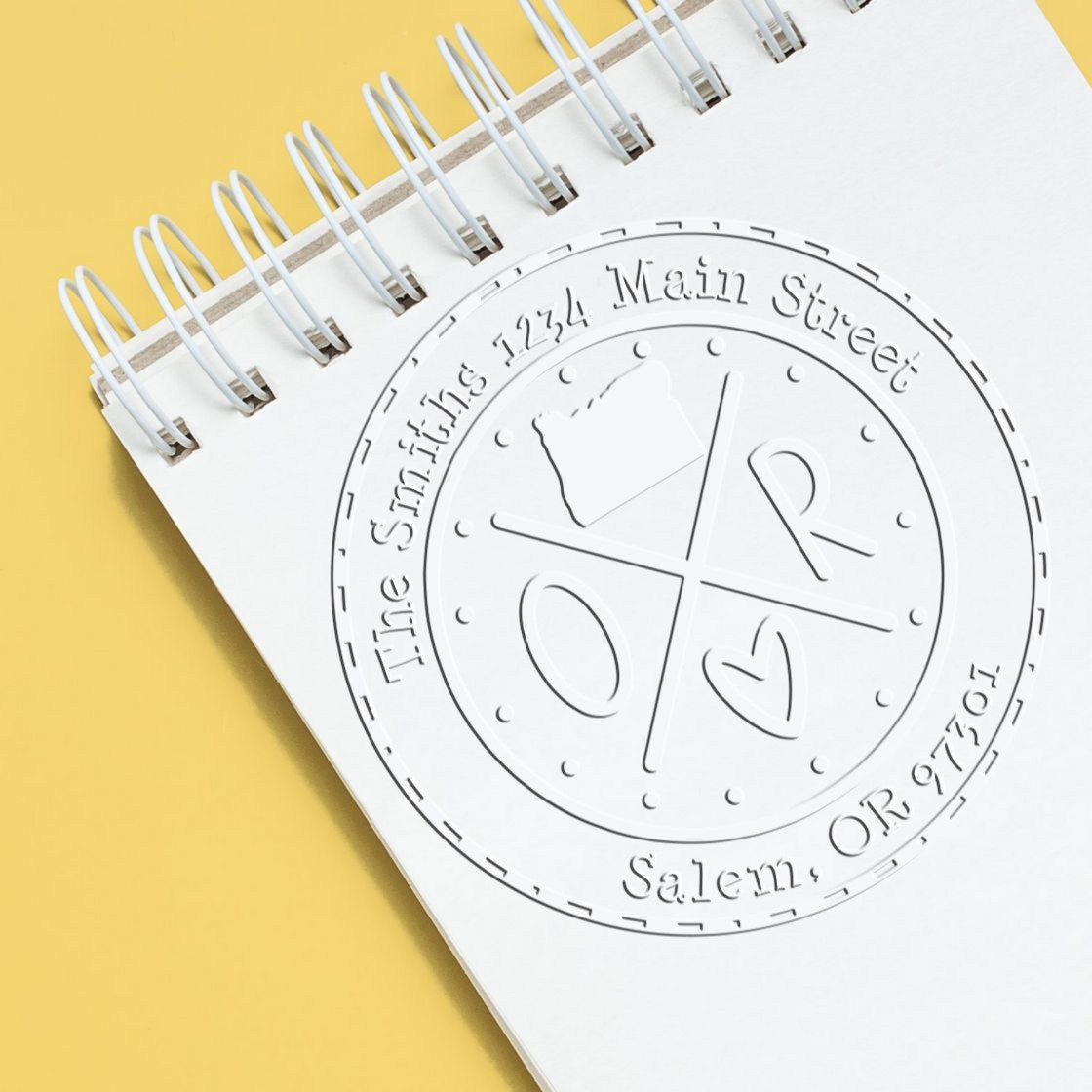 White spiral notebook with embossed circular stamp seal design, featuring Salem, Oregon and 2026 text on a yellow background.