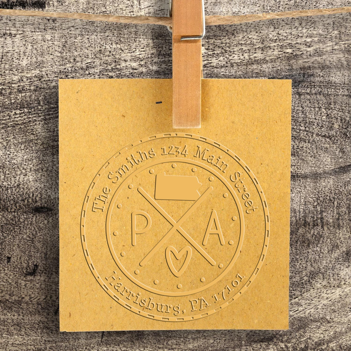 Gold embossed custom stamp and seal for The Smiths, with Harrisburg, PA text, hanging on a wooden clip against gray wood.
