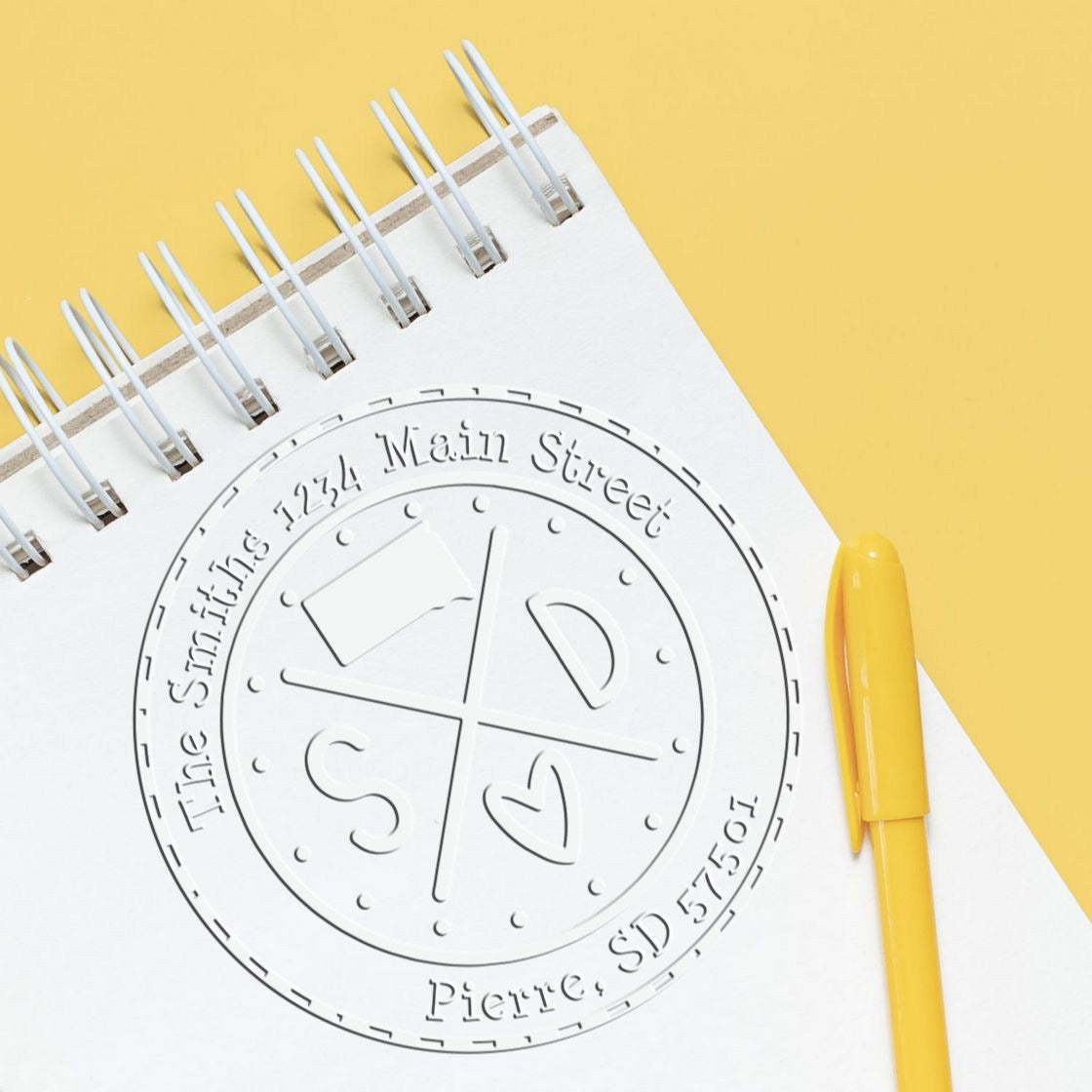 Custom embossing stamp and seal on a white spiral notebook with a yellow pen against a yellow background.