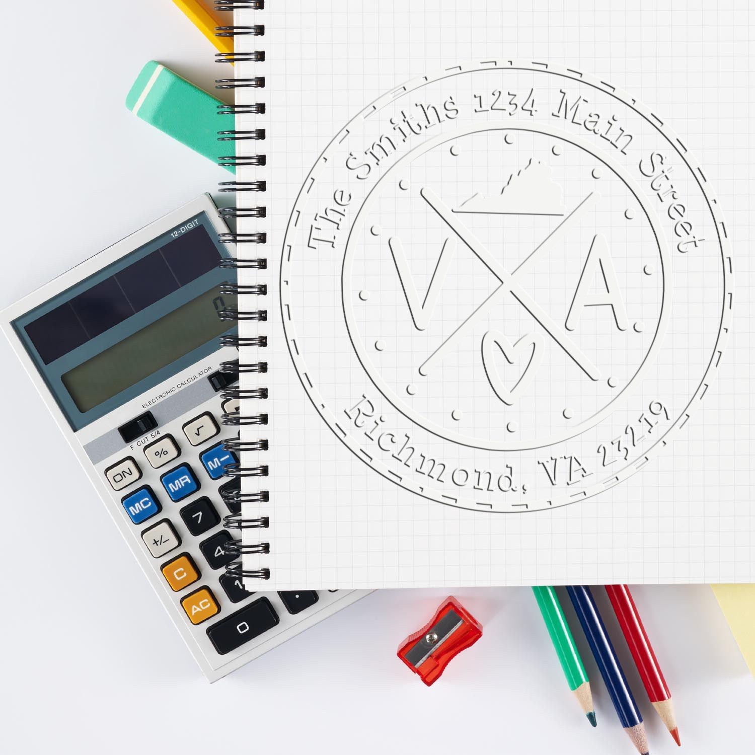 White embossed VXA seal stamp on graph notebook, beside a calculator, colored pencils, eraser and sharpener.