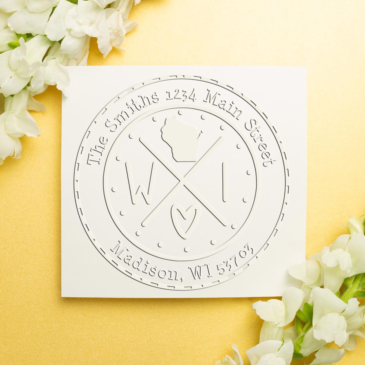 Round white embossed custom stamp and seal with address text, on a pale yellow background with white flowers.