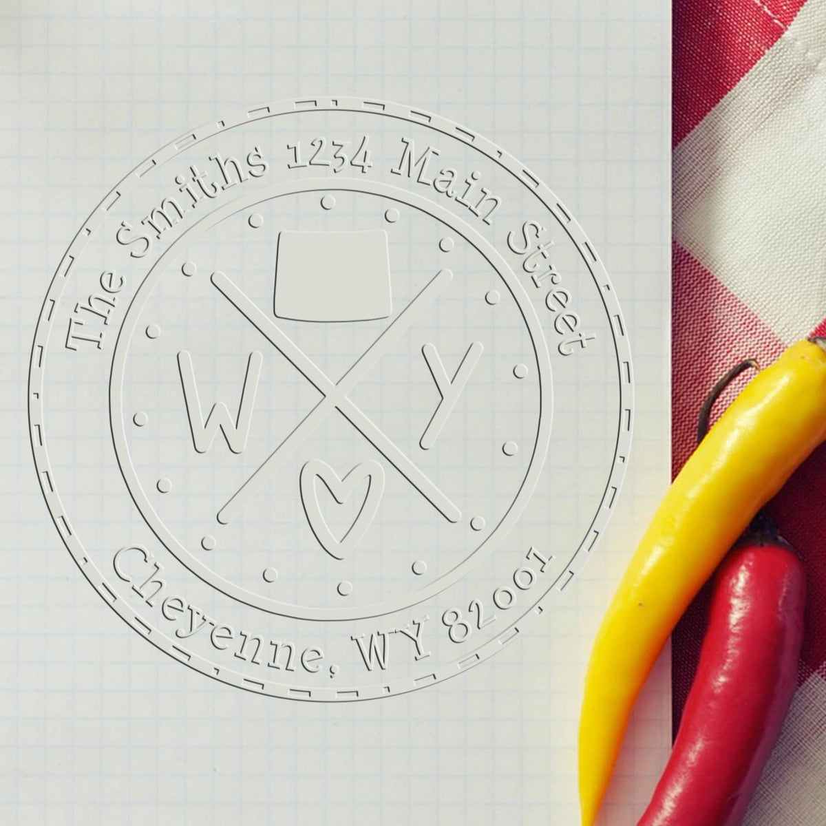 Custom round embossing seal with silver lettering on white paper, beside red and yellow stamp handles.