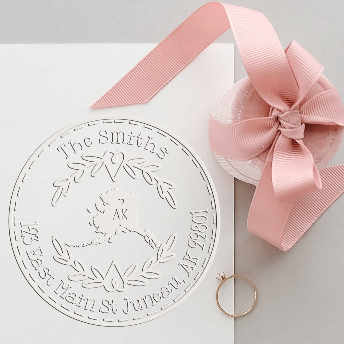White custom stamp and wax seal with pink ribbon, engraved family crest, and rose-gold ring.