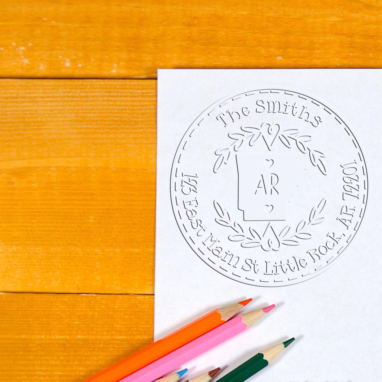 White embossed stamp and seal proof with The Smiths circular wreath, on orange wood with pink, orange, and green pencils.