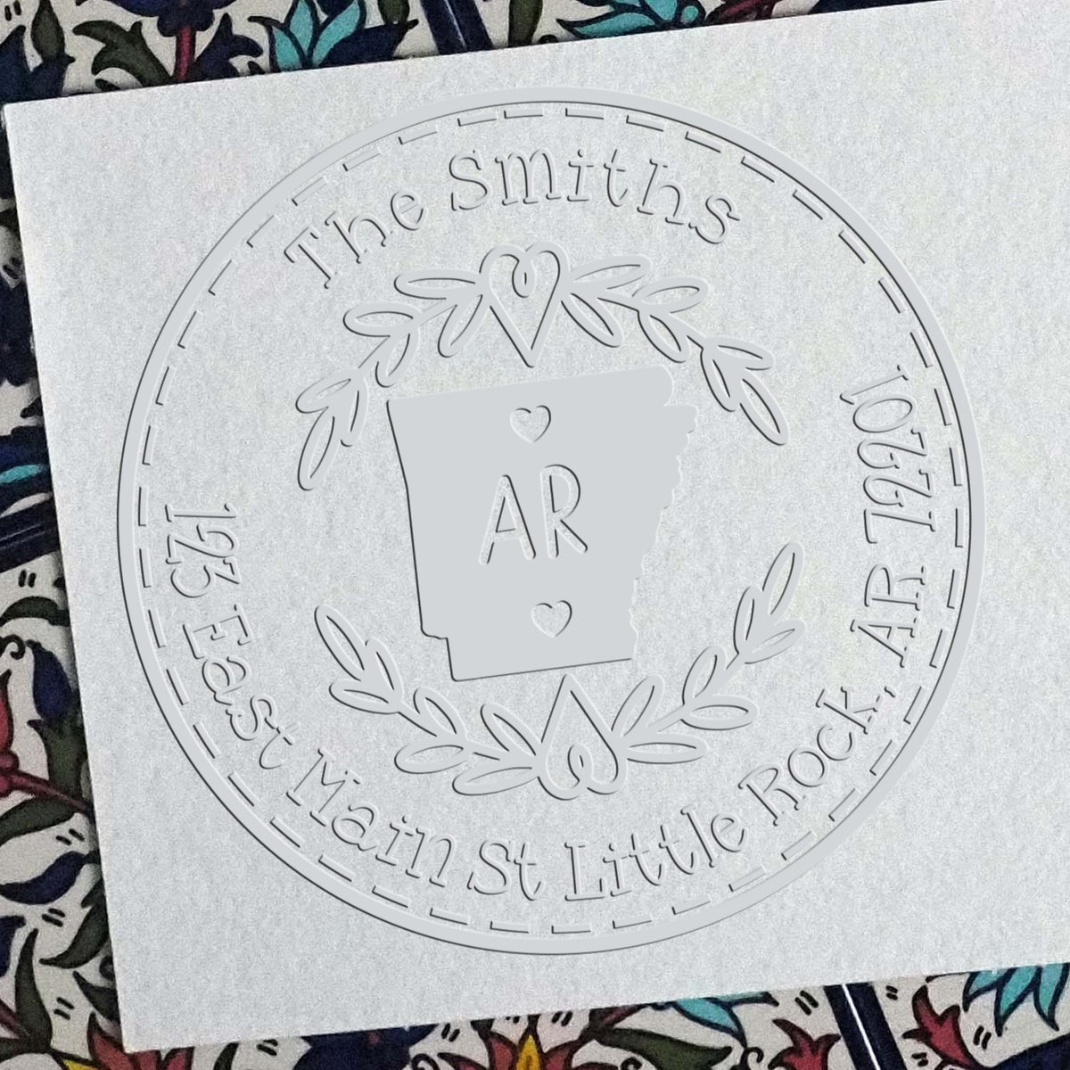 White embossed circular stamp seal for The Smiths, with Arkansas outline, AR initials, hearts, laurel wreath, and address text.