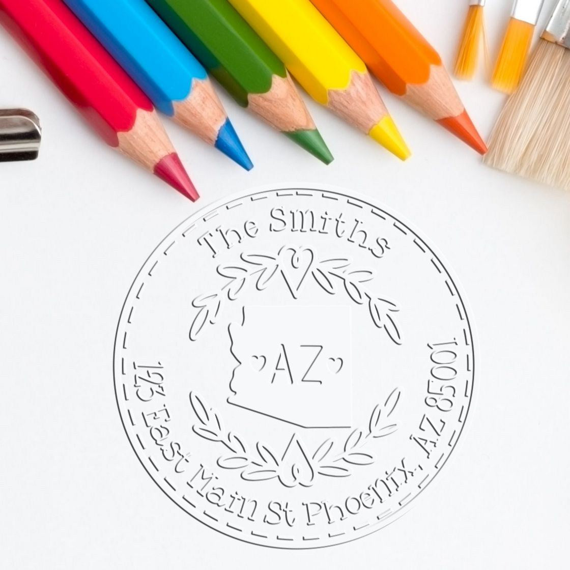 Custom embossing seal stamp with rainbow pencils and brushes, featuring a circular monogram and Arizona address.